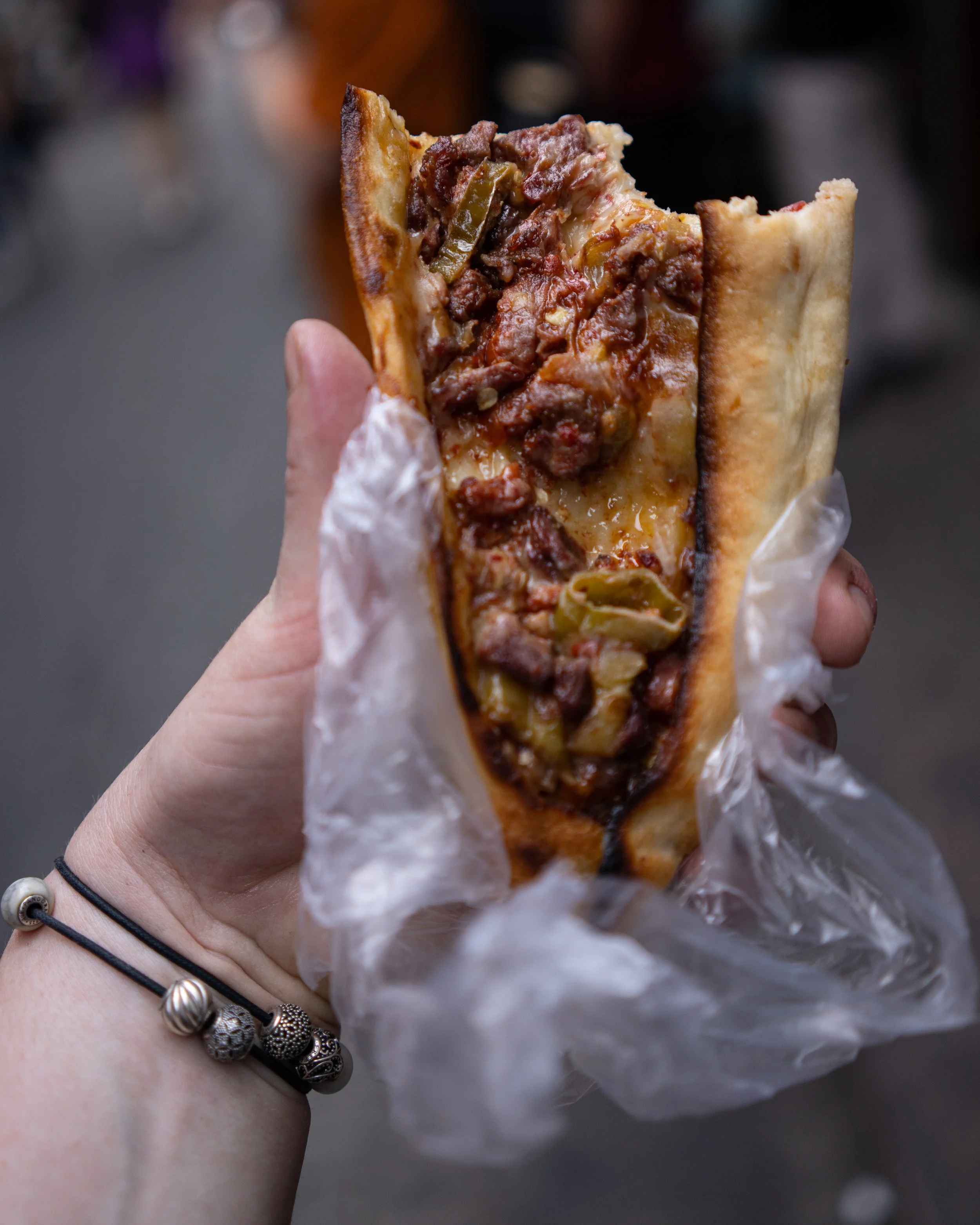 Half a pide is held out to the camera. The pide is stuffed full of melted cheese and minced meat taken on the streets of Istanbul.