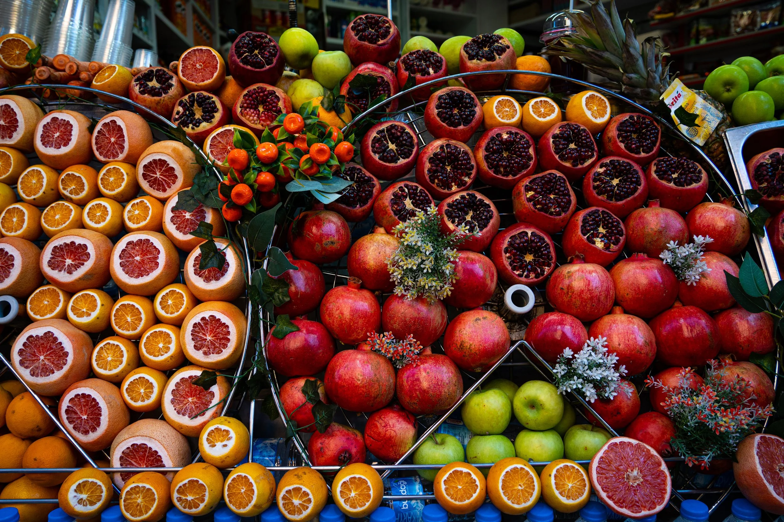 A fruit juice stall is decorated with oranges, apples and pomegranates stacked up on circular metal plates.
