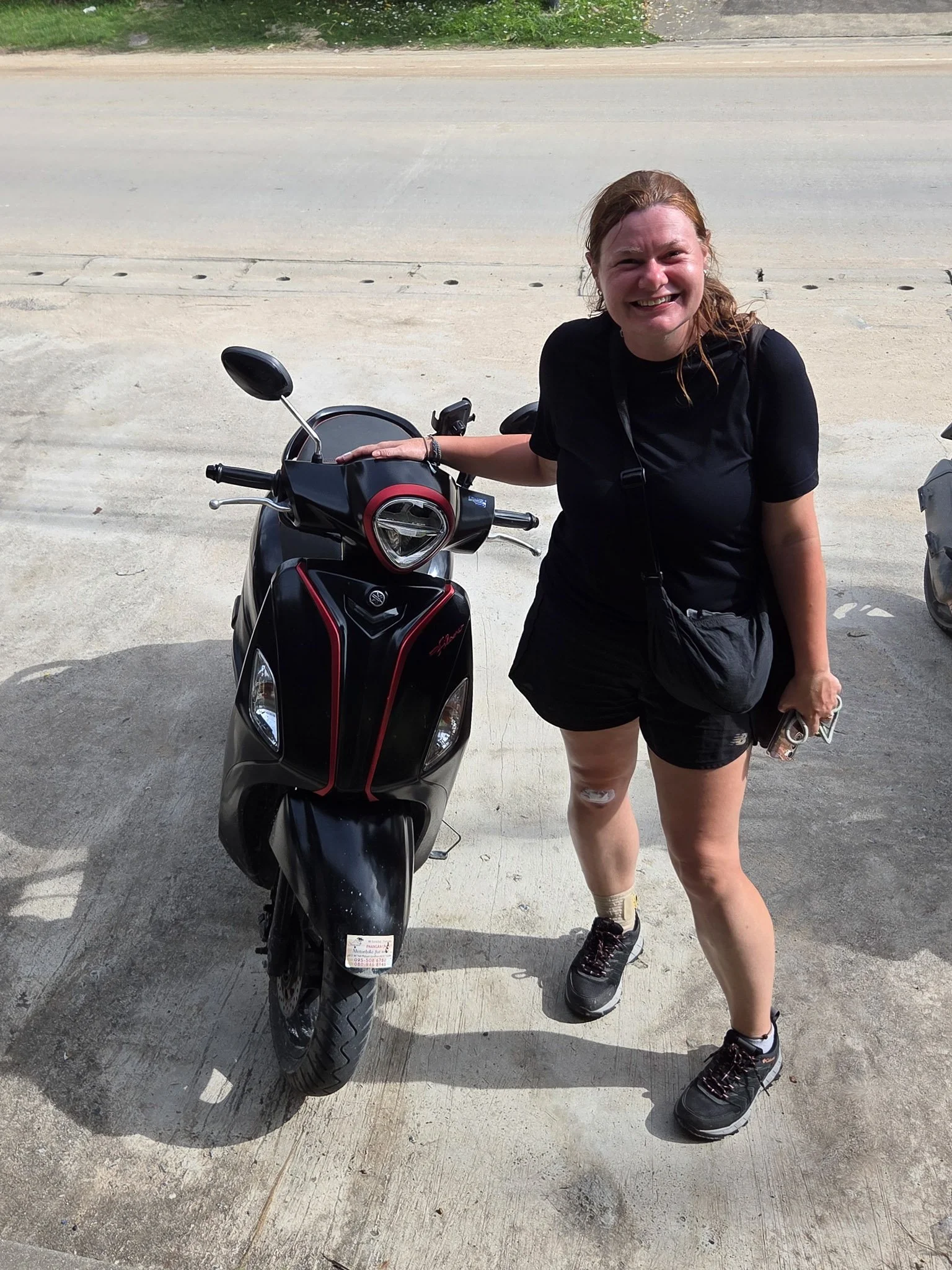 Ellie smiles to the camera whilst posing next to her rented black and red Yamaha Filano scooter.