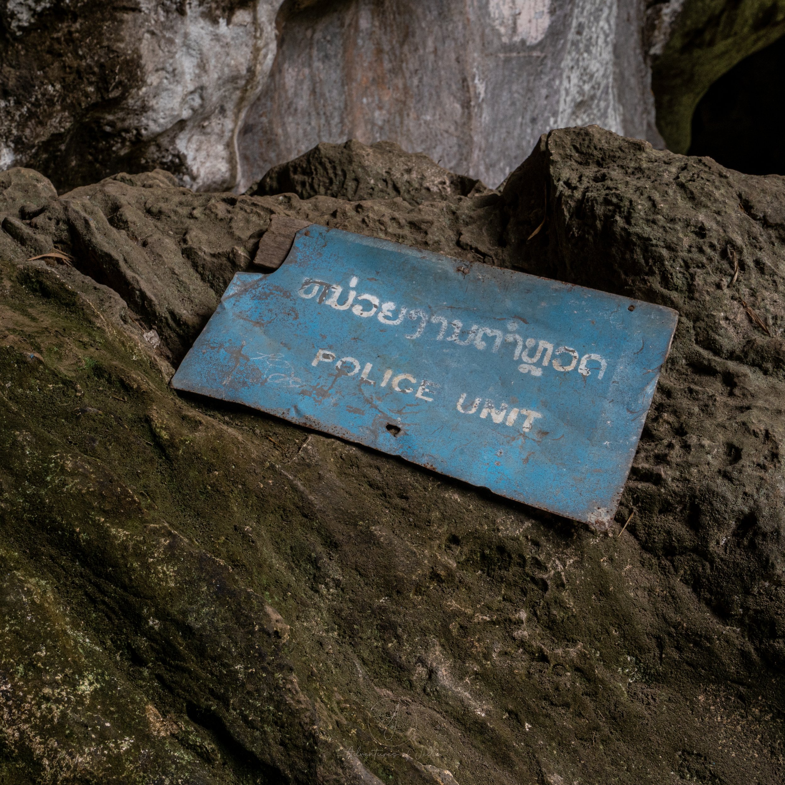 A blue sign lies on a rock saying "Police Unit" in English and Laotian script. This sign is found in cave one of the Phathok Cave System in Nong Khiaw, Laos.