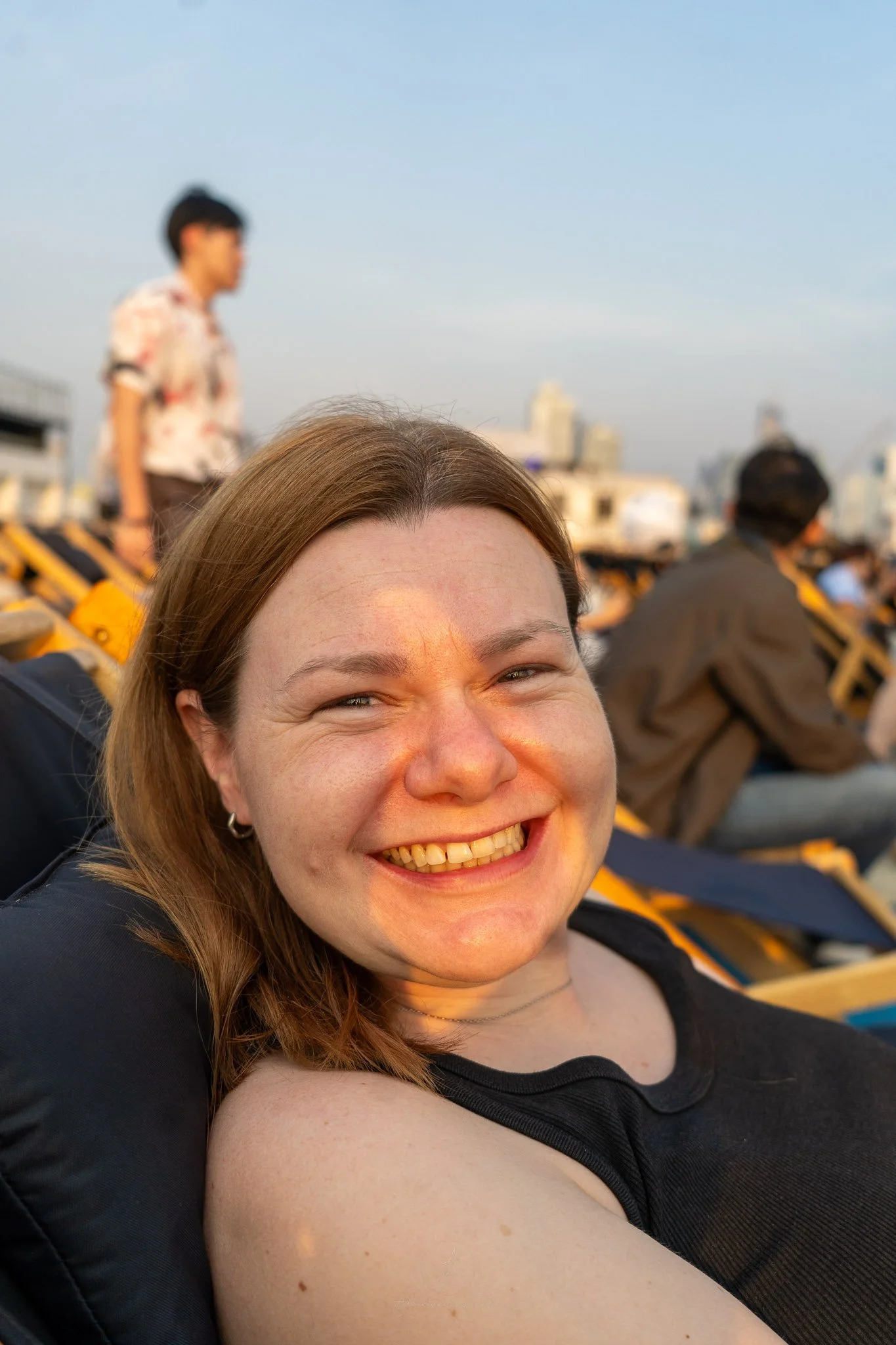 Ellie smiles at the camera whilst sitting in a black deckchair on top of Rivercity ready for the Skyline Film event.