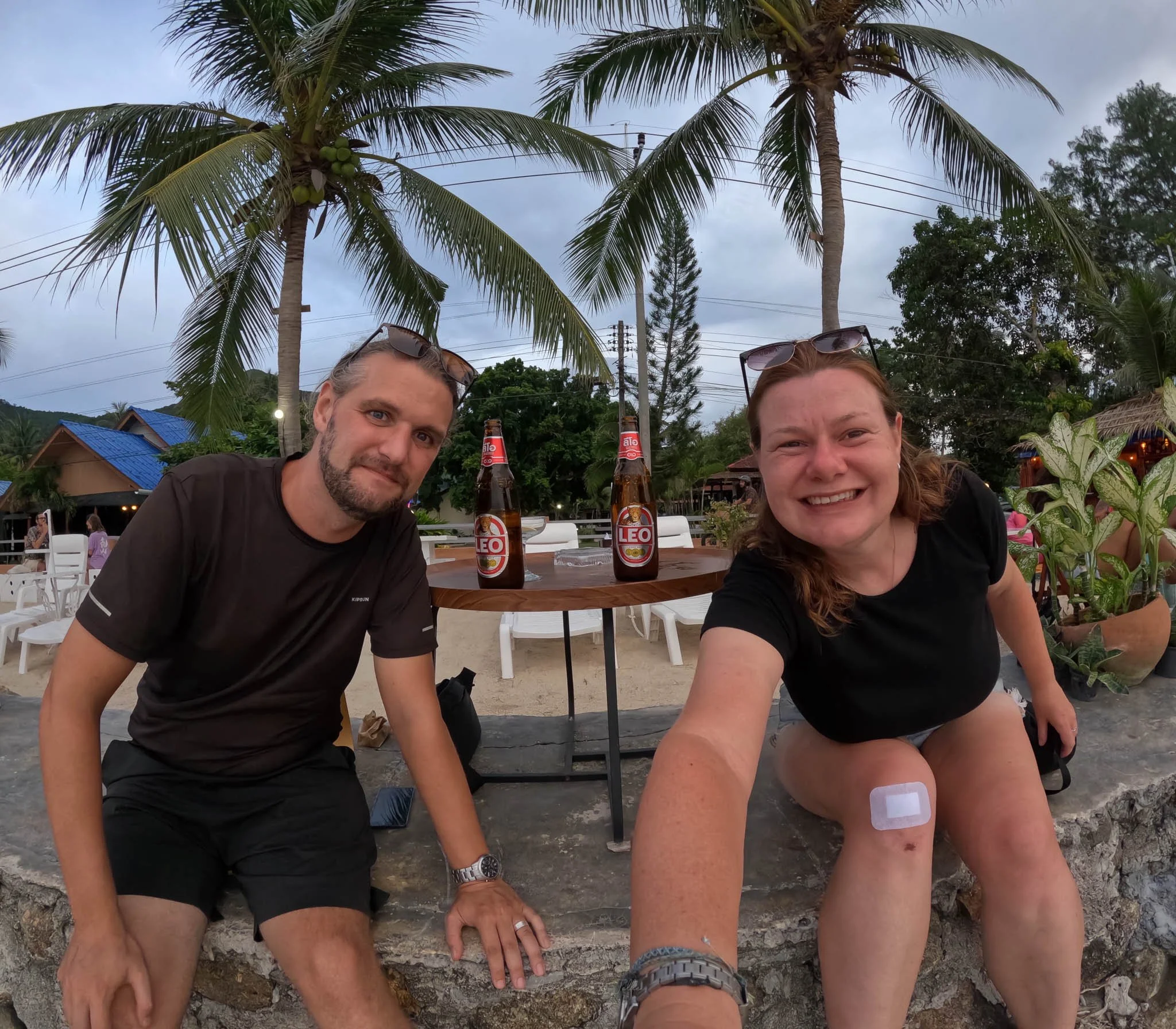 Adventures of Jellie pose for a selfie at a beach bar on Chaloklum Beach, Koh Phangan. Behind them on the table sit two bottles of Leo beer.