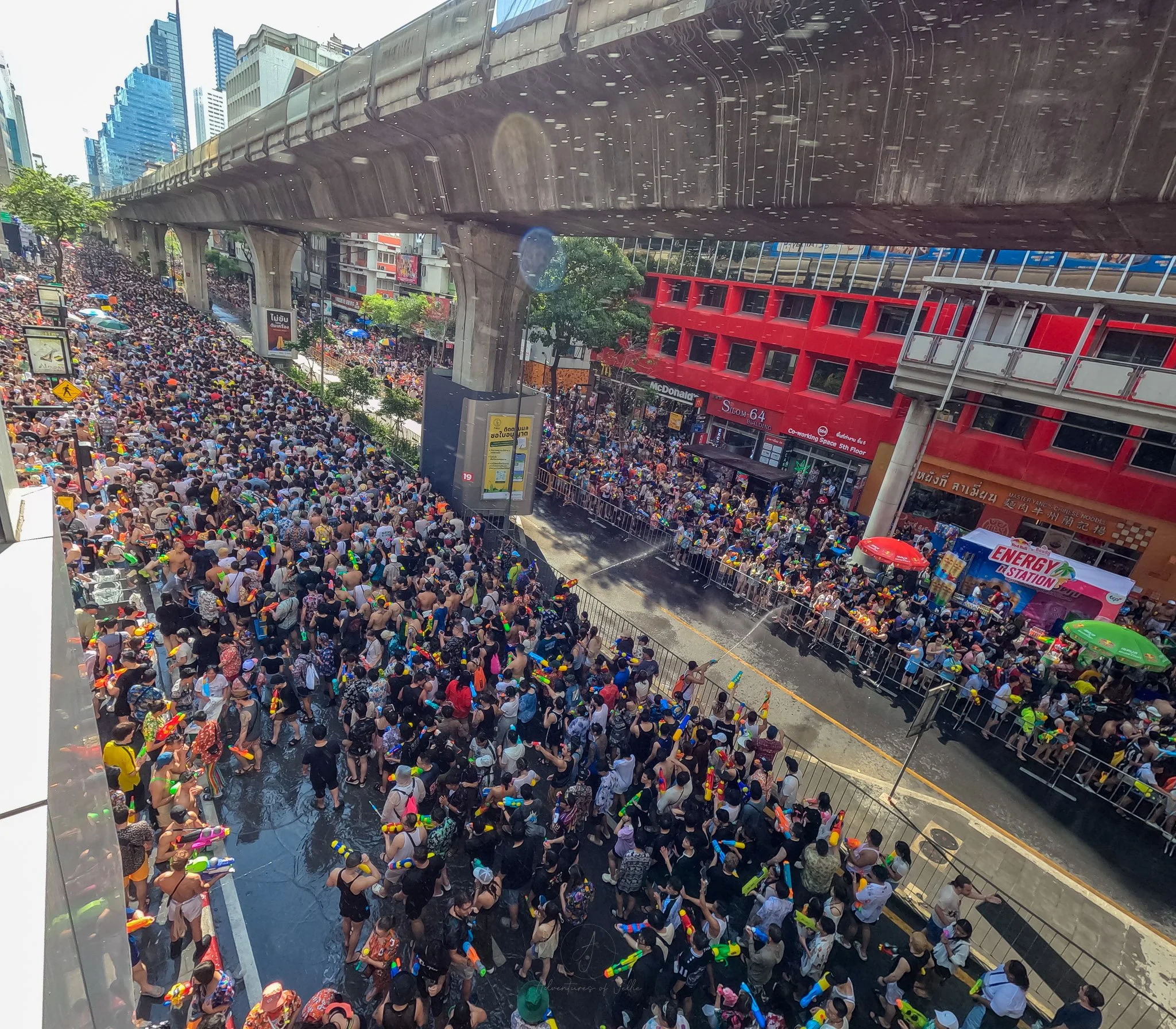 Enormous crowds spray each other with waterguns as they make their way down crowded roads under an MRT line in Bangkok.