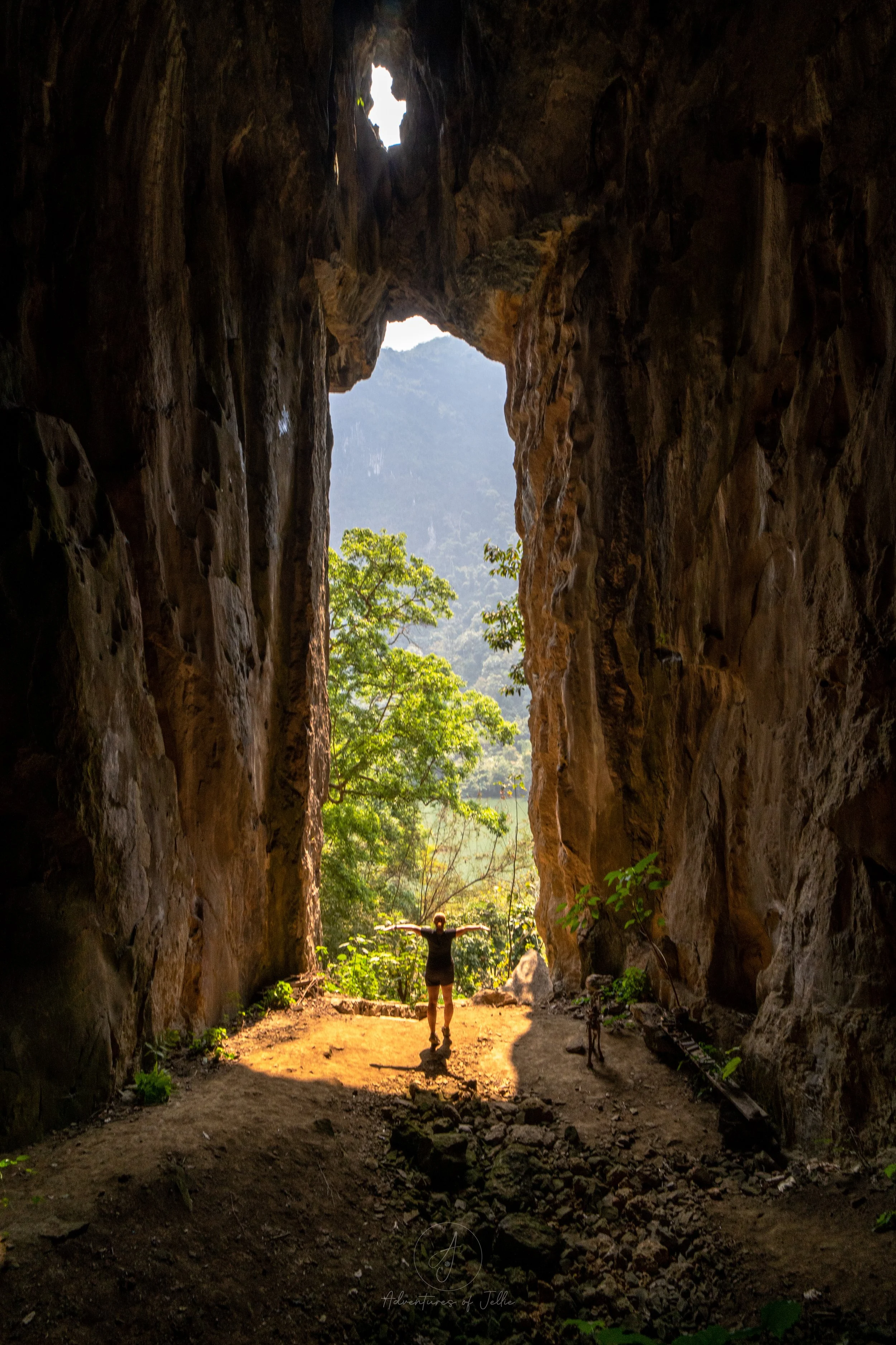 Ellie stands with outstretched arms, dwarfed by an enormous cave opening inside the Pha Kuang Cave, Nong Khiaw in Laos.