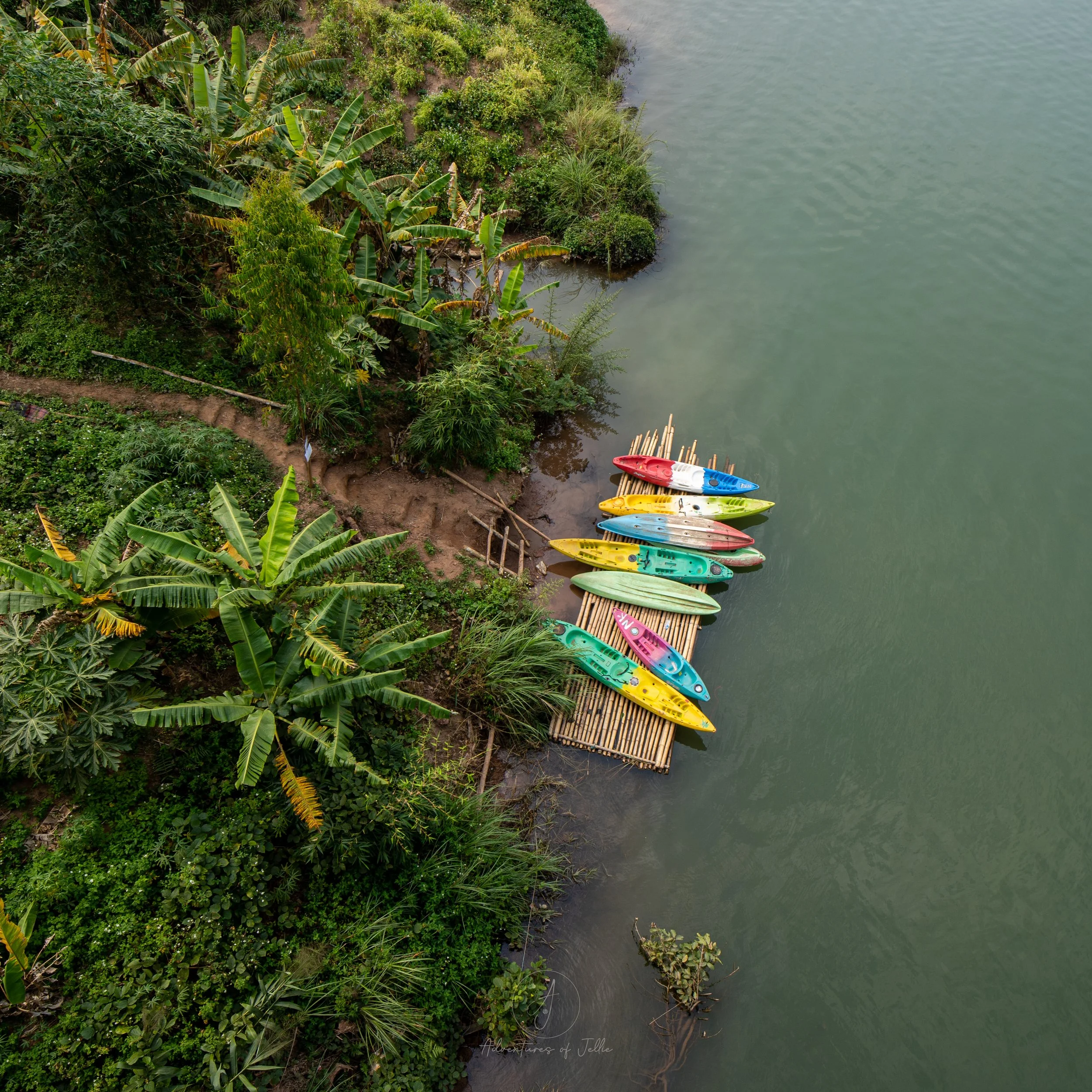Eight colourful kayaks sit moored to a bamboo pier on the Nam Ou river. Photo taken from a top down perspective taken from Nong Khiaw's Bridge.