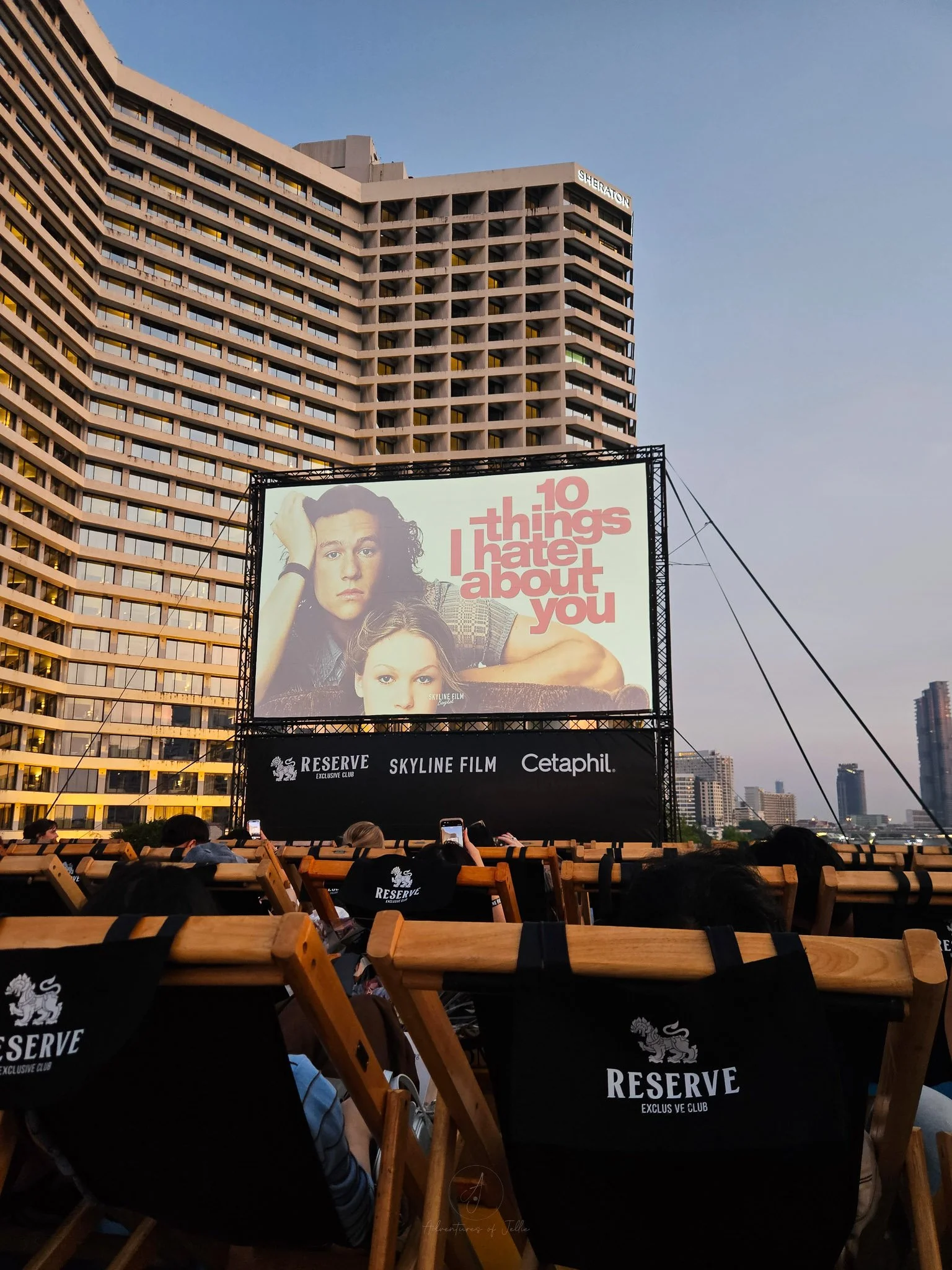 Heath Ledger and Julia Stiles appear on a cinema screen next to red writing which says "10 Things I Hate About You" at a film screening on top of Rivercity. In front deck chairs sit in rows and behind the Sheraton Hotel rises up