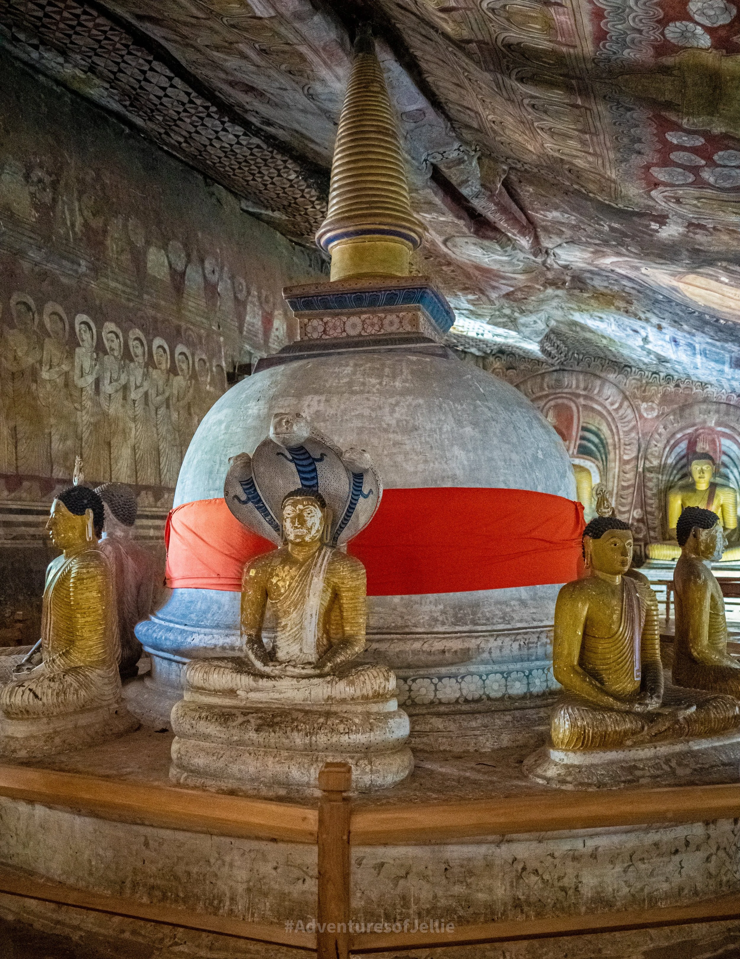 A stupa clad in orange and surrounded by Buddha and Naga statues in the Dambulla Royal Cave Temple