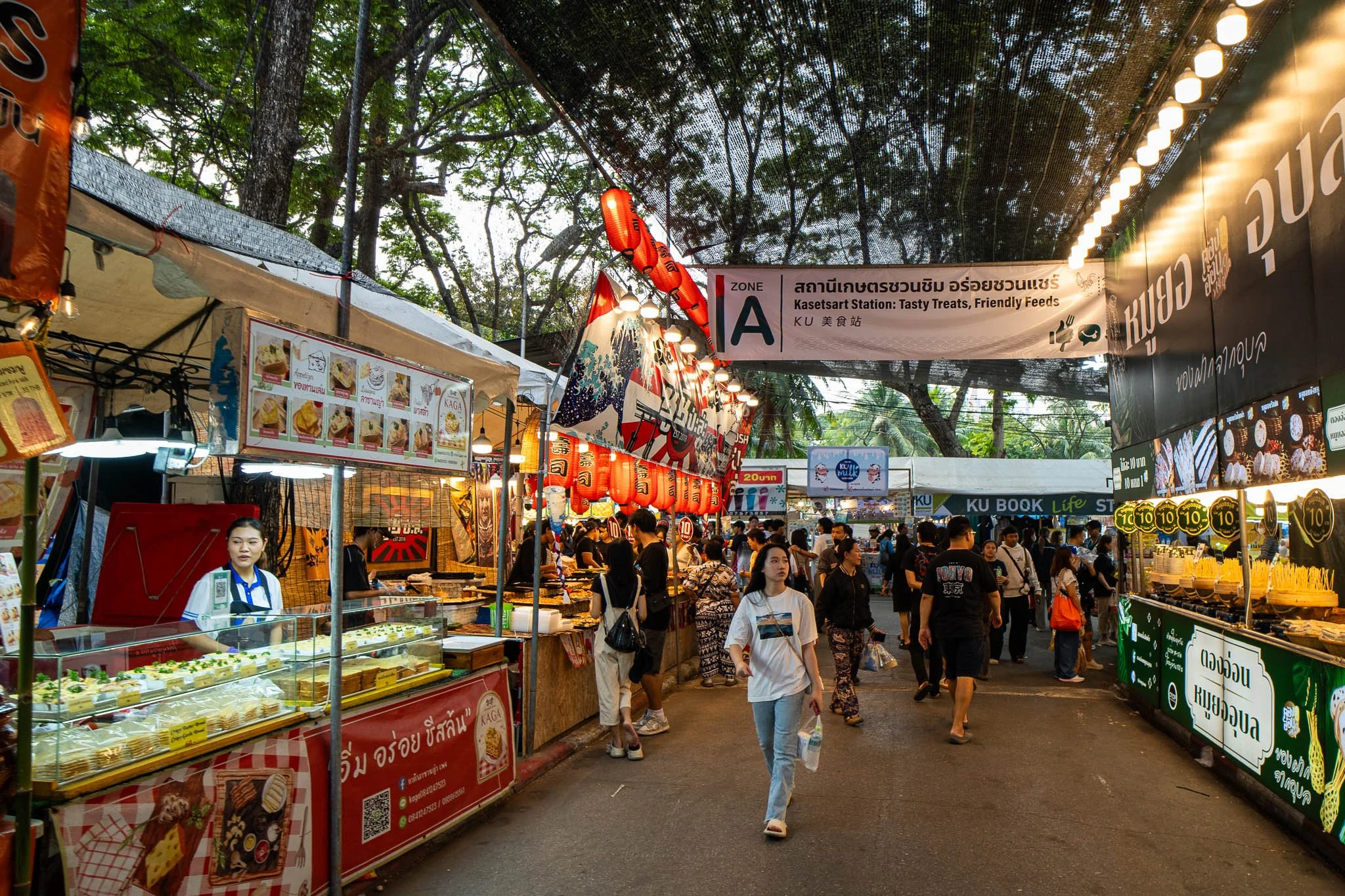 Crowds of people walk along a road lined with street food stalls at the Kaset Fair in Bangkok.