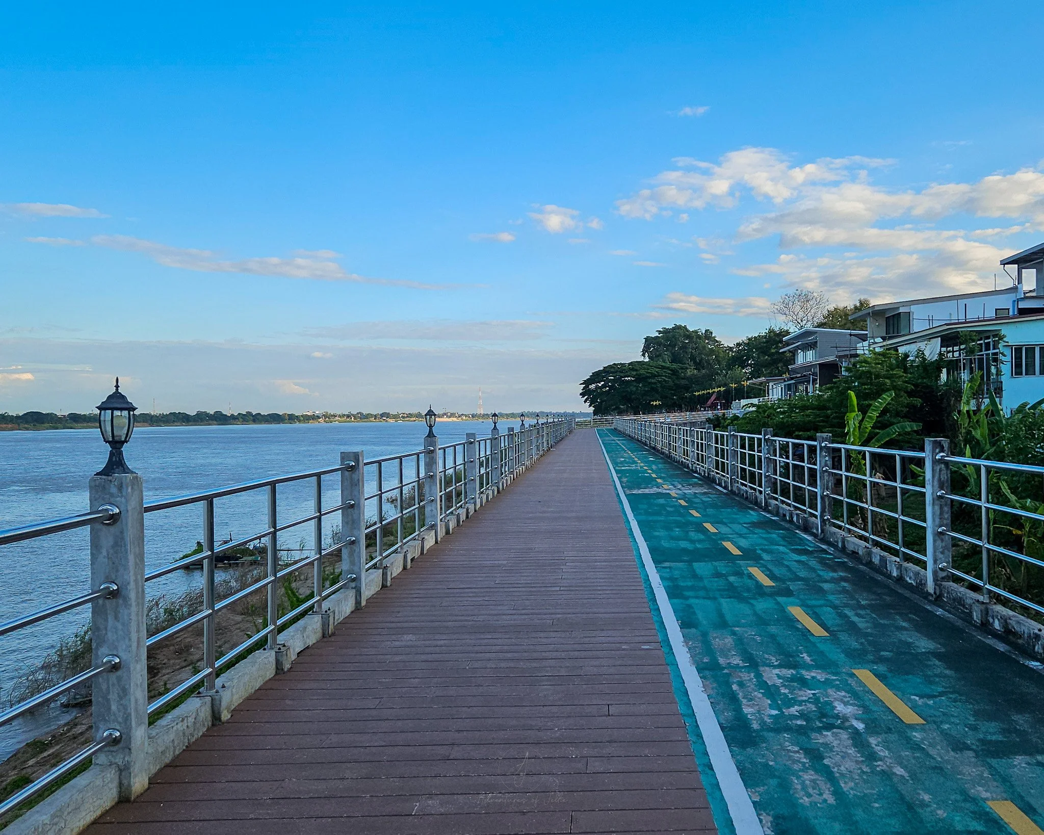 A view down the riverfront walkway and cycle path. The cycle path is green with road markings and the walkway sits out above the river.