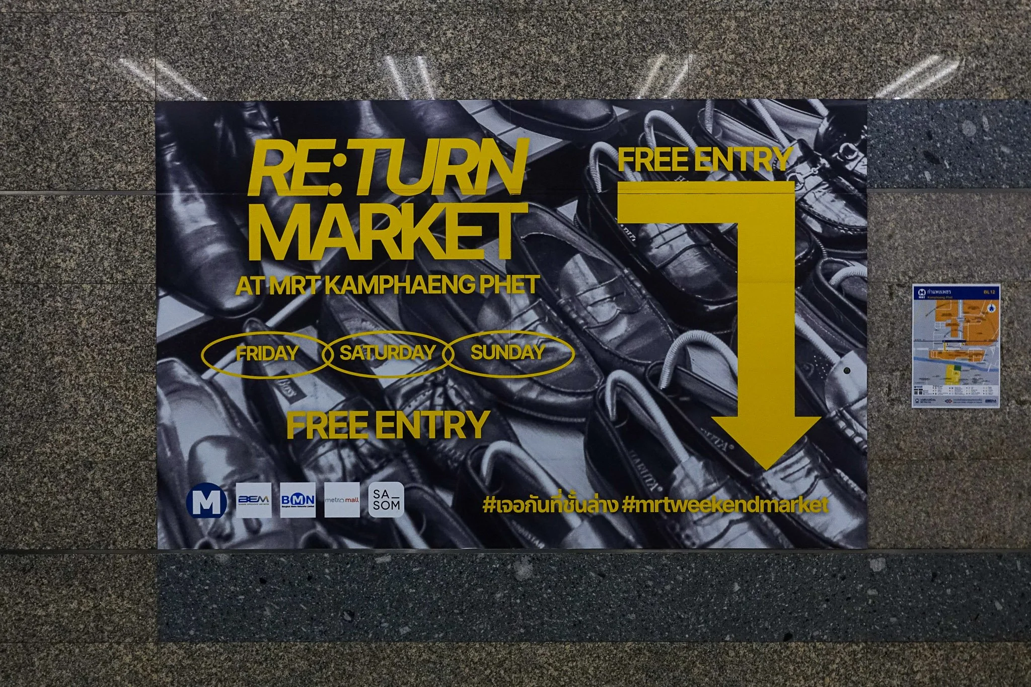 A huge black and white poster with yellow text saying "Re:Turn Market at MRT Kamphaeng Phet. Friday, Saturday, Sunday. Free Entry" hangs on the marble wall of an MRT station in Bangkok.