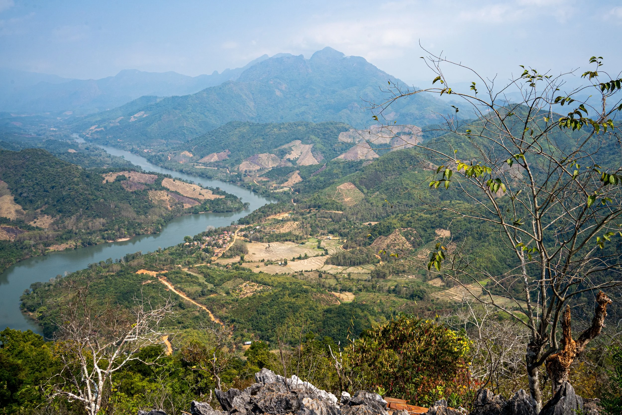 A view from the top of the Pha Daeng hike down over the curving Nam Ou River, golden paddy fields, forest and mountains in northern Laos.