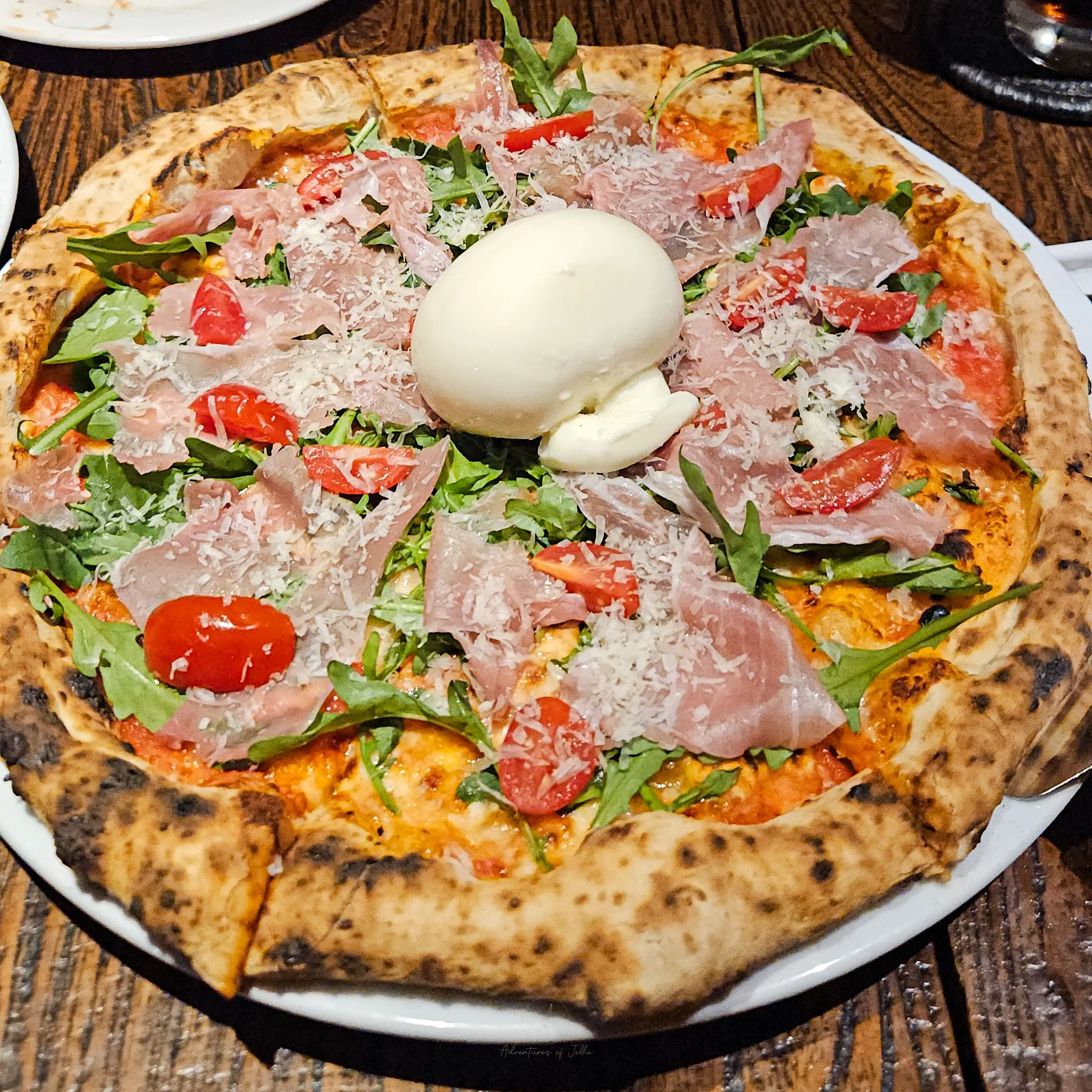 A thin crust sourdough pizza is topped with a ball of burrata cheese, slices of parma ham, rocket, sliced tomatoes and grated parmesan at the Long Pizza Restaurant in Khon Kaen, Thailand.