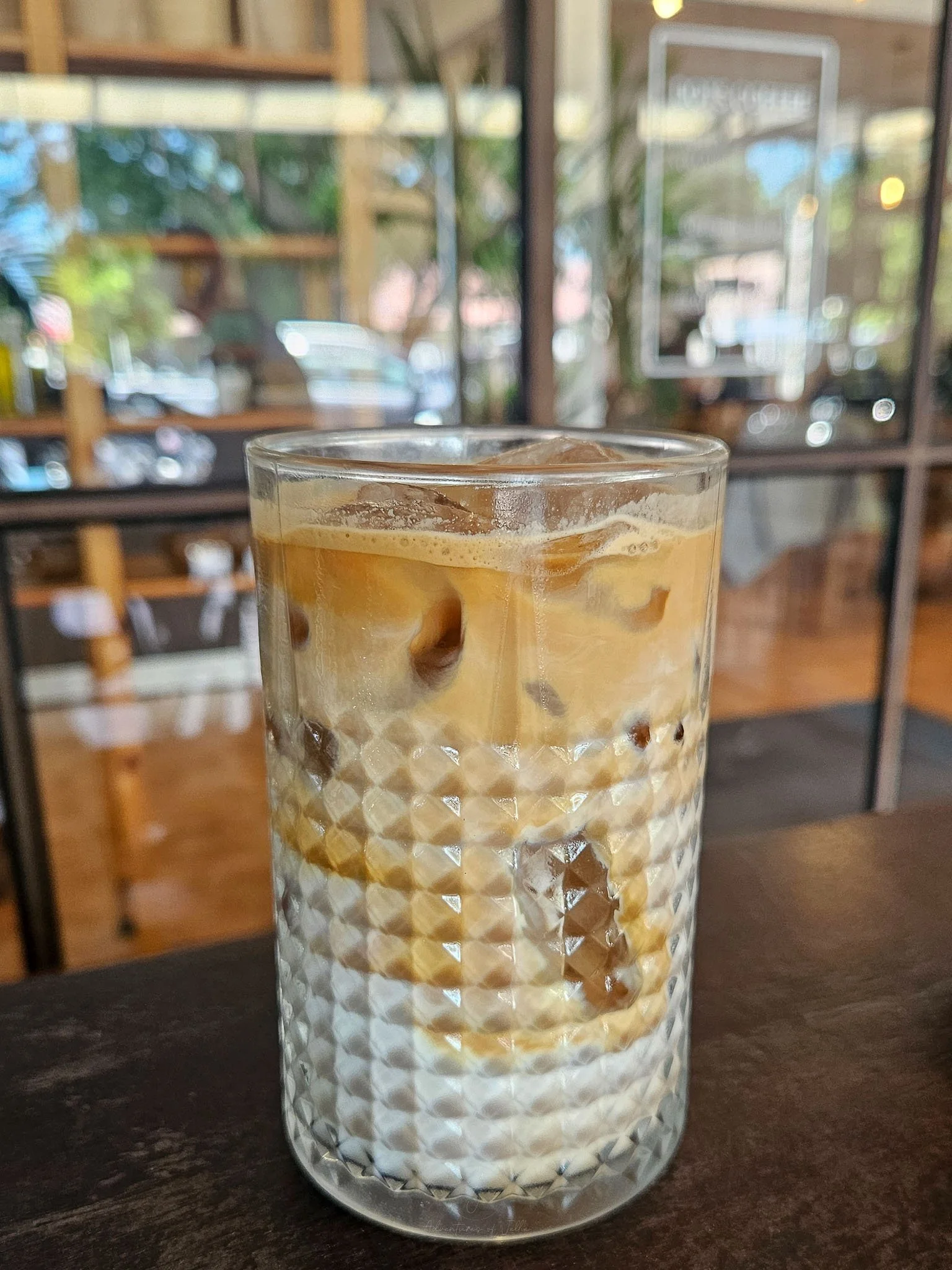 A glass of iced latte sits on a wooden table outside the Dots Cafe on Koh Phangan.
