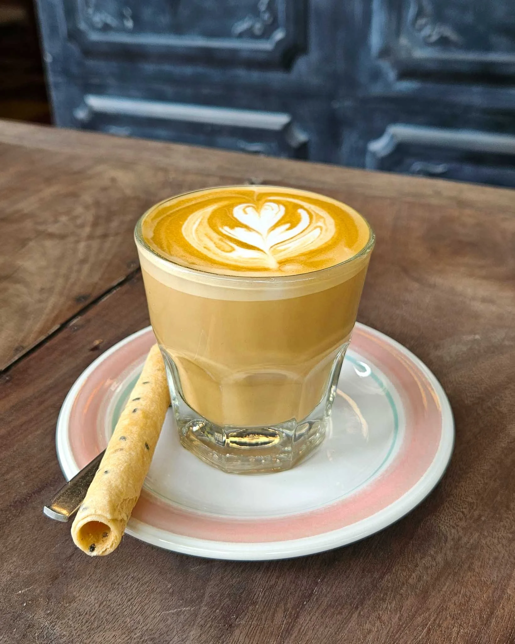On top of a pink and white saucer sits a flat white coffee and a sesame seed tuile at the Cafe Espresso Roaster in Kampot.