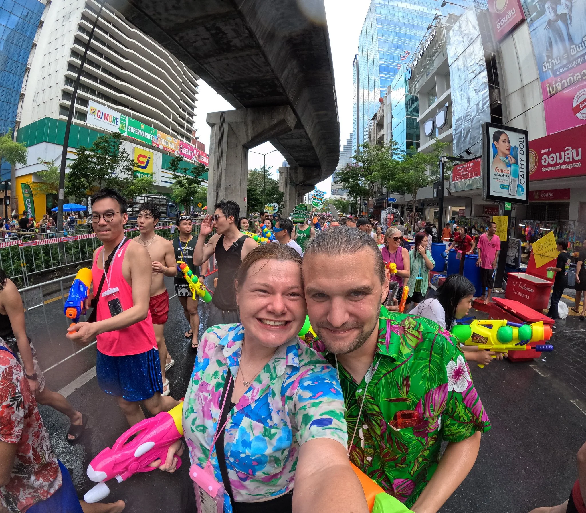A soaked Jellie smile for the camera, behind them people aim their waterpistols at them.