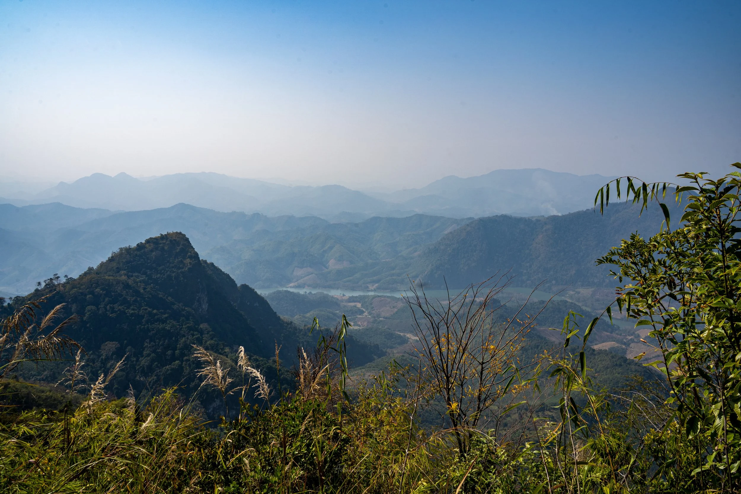 Rows of mountains stretch off towards the horizon as the path nears the peak of the Pha Kao viewpoint trail in Nong Khiaw, Laos.