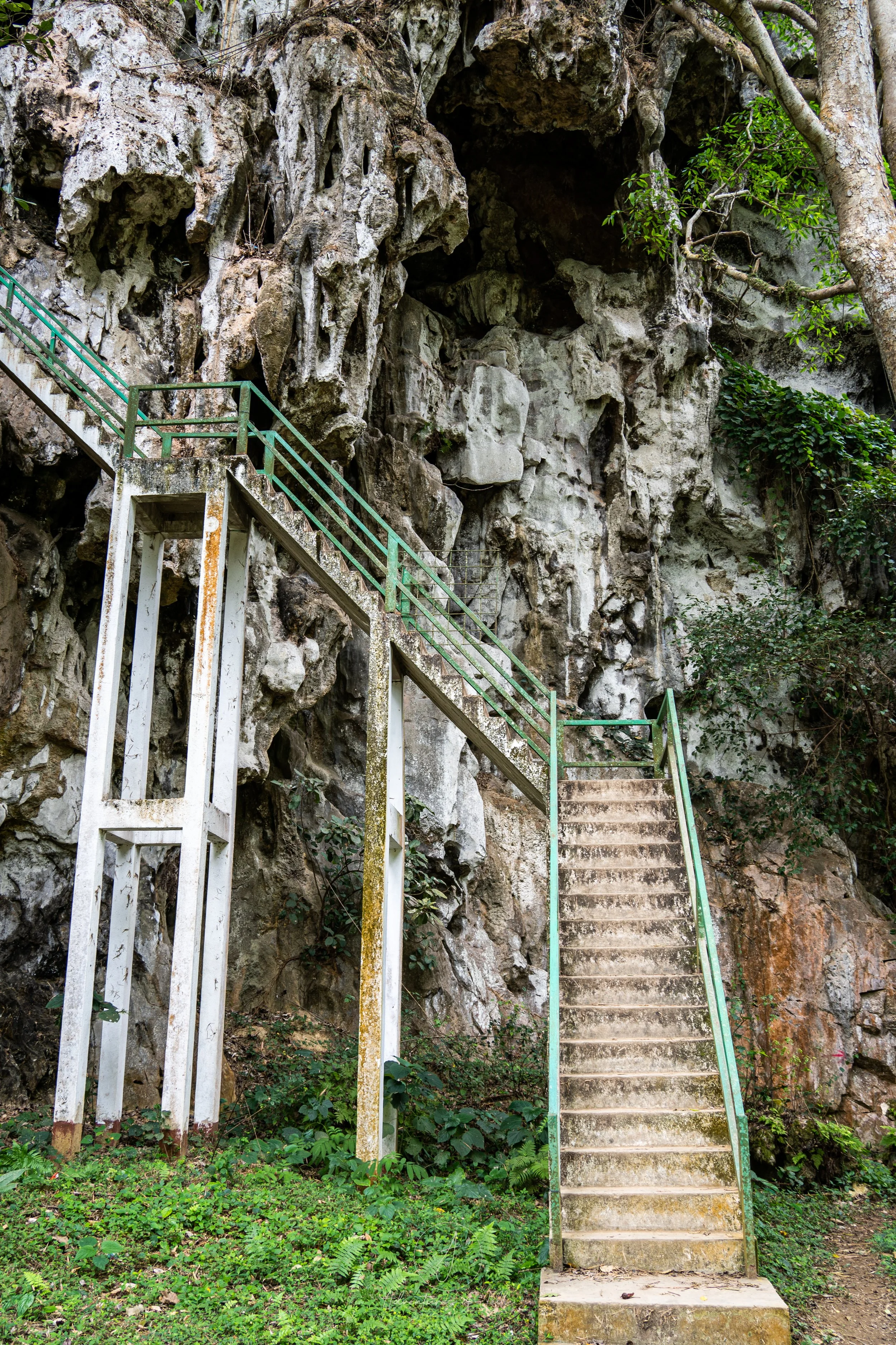 A concrete staircase with green railings marks the way up to one of the Phathok Caves in Nong Khiaw, Laos.