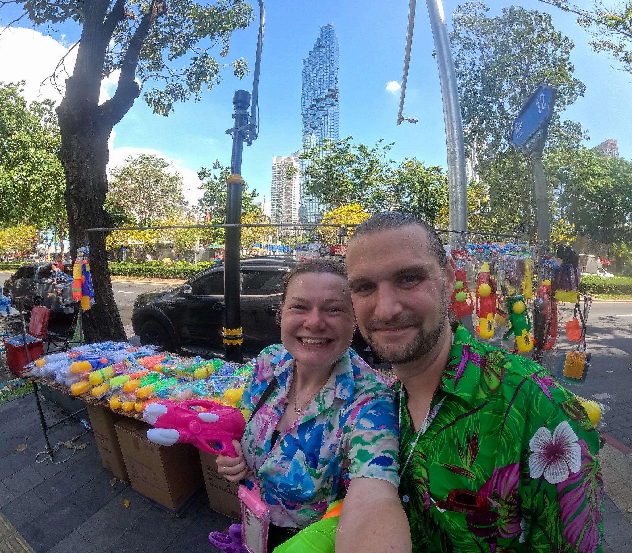 John and Ellie smile next to a stall completely full of waterguns for sale.