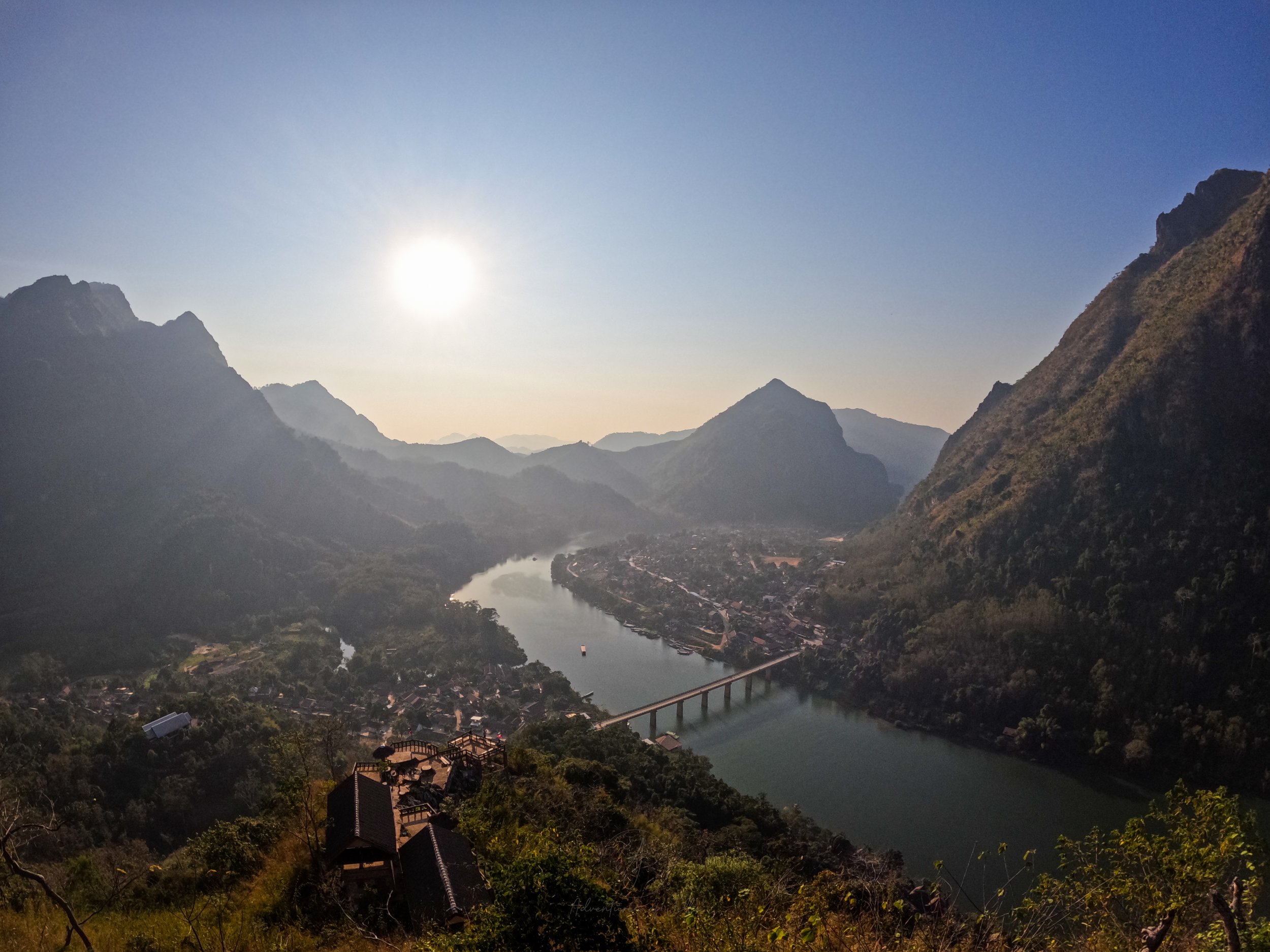 A view over the setting sun, mountain peaks, Nong Khiaw town and the curving Nam Ou River as seen from the viewing platform at the top of the Som Nang trail.