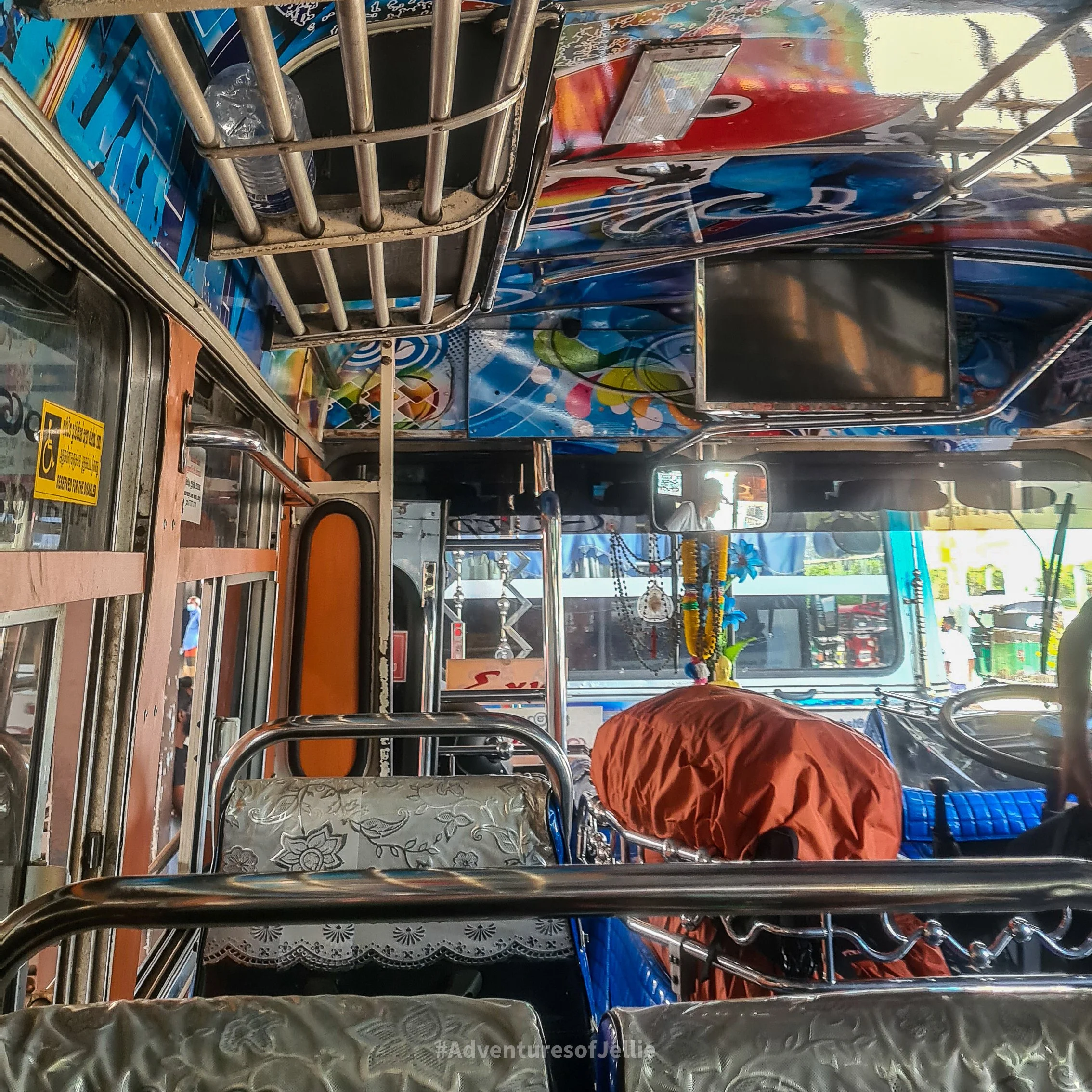 The colourful interior of a local Sri Lankan bus. In front, two rows of seat stretch away to the windscreen. Next to the driver's seat sits an orange coloured backpack.