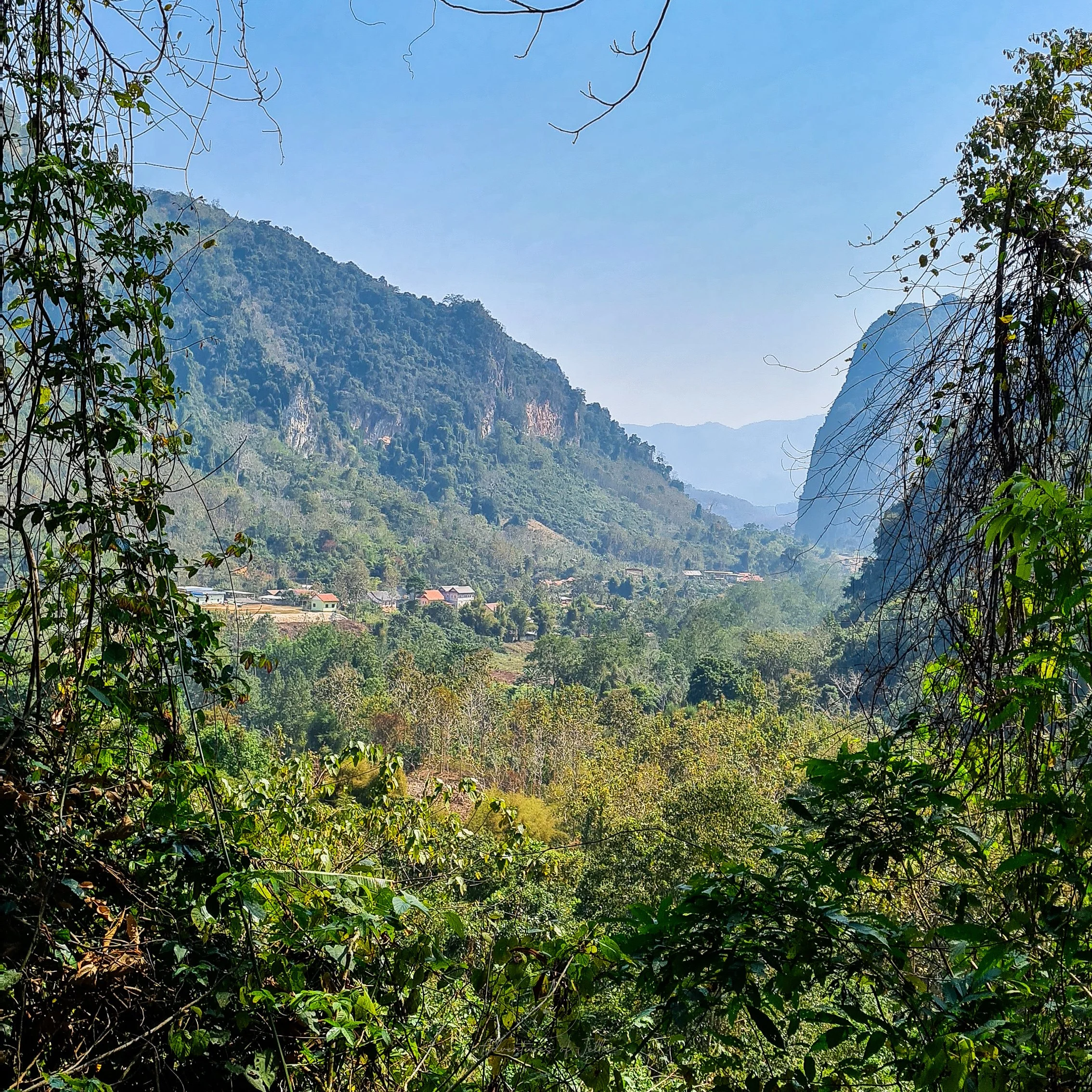 Outside the Phar Noi History Caves the green forested landscape of Nong Khiaw rolls away towards a mountainous horizon.