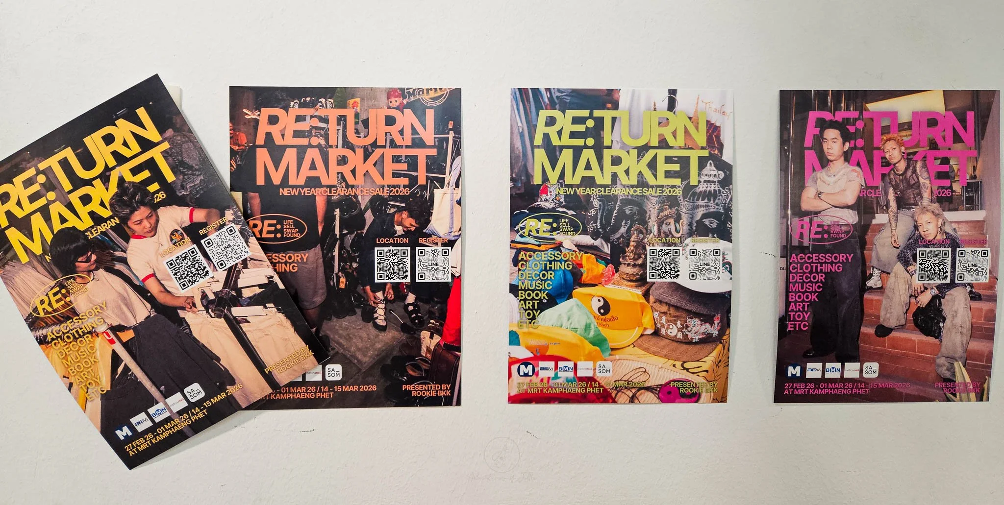 A row of colourful posters are stuck to a white painted wall advertising the Re:Turn Market in Bangkok.