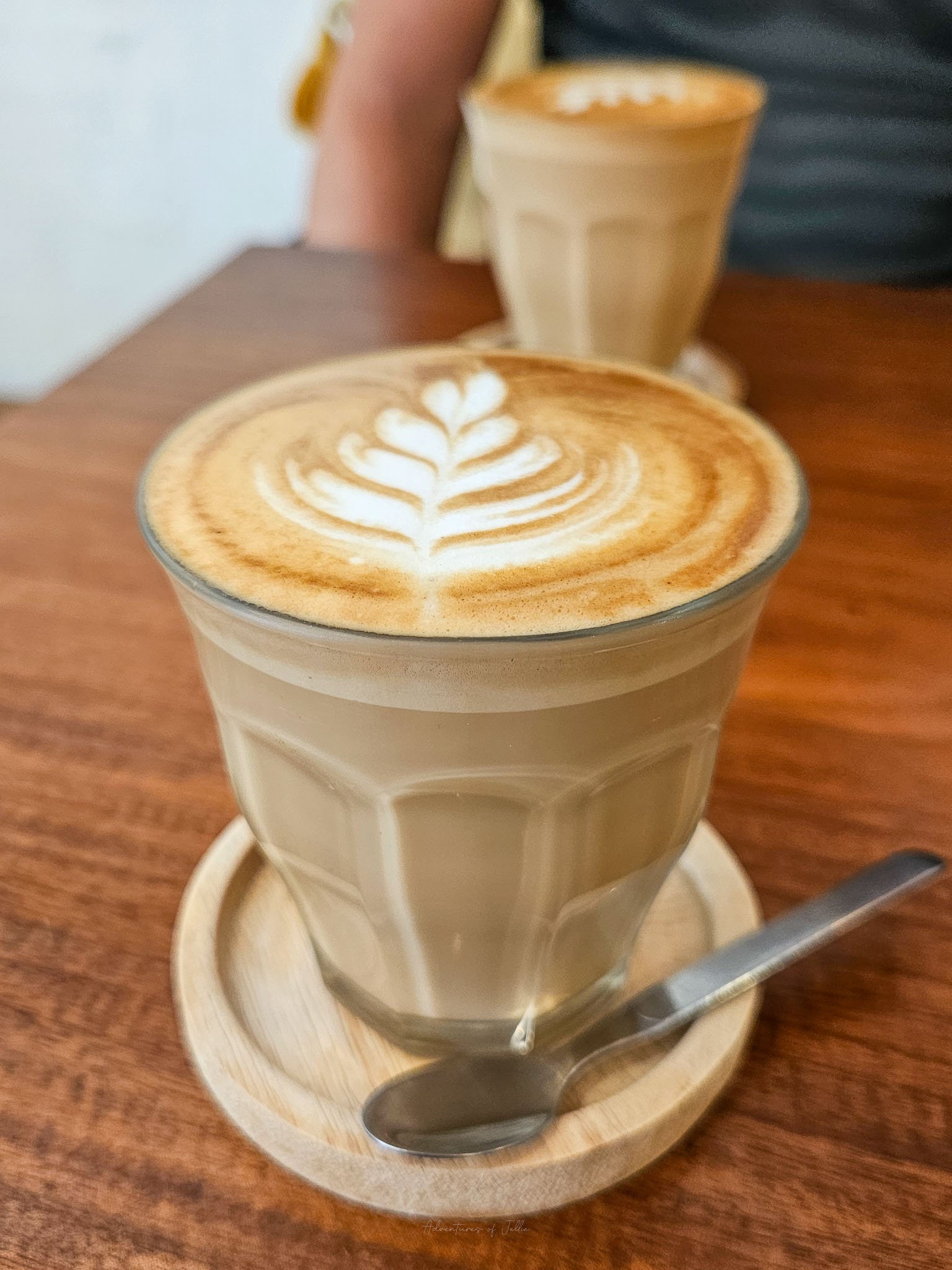 Sitting on a wooden table on top of circular wooden coasters are two cups of hot flat white coffee at the Brew Co Cafe of Koh Phangan.
