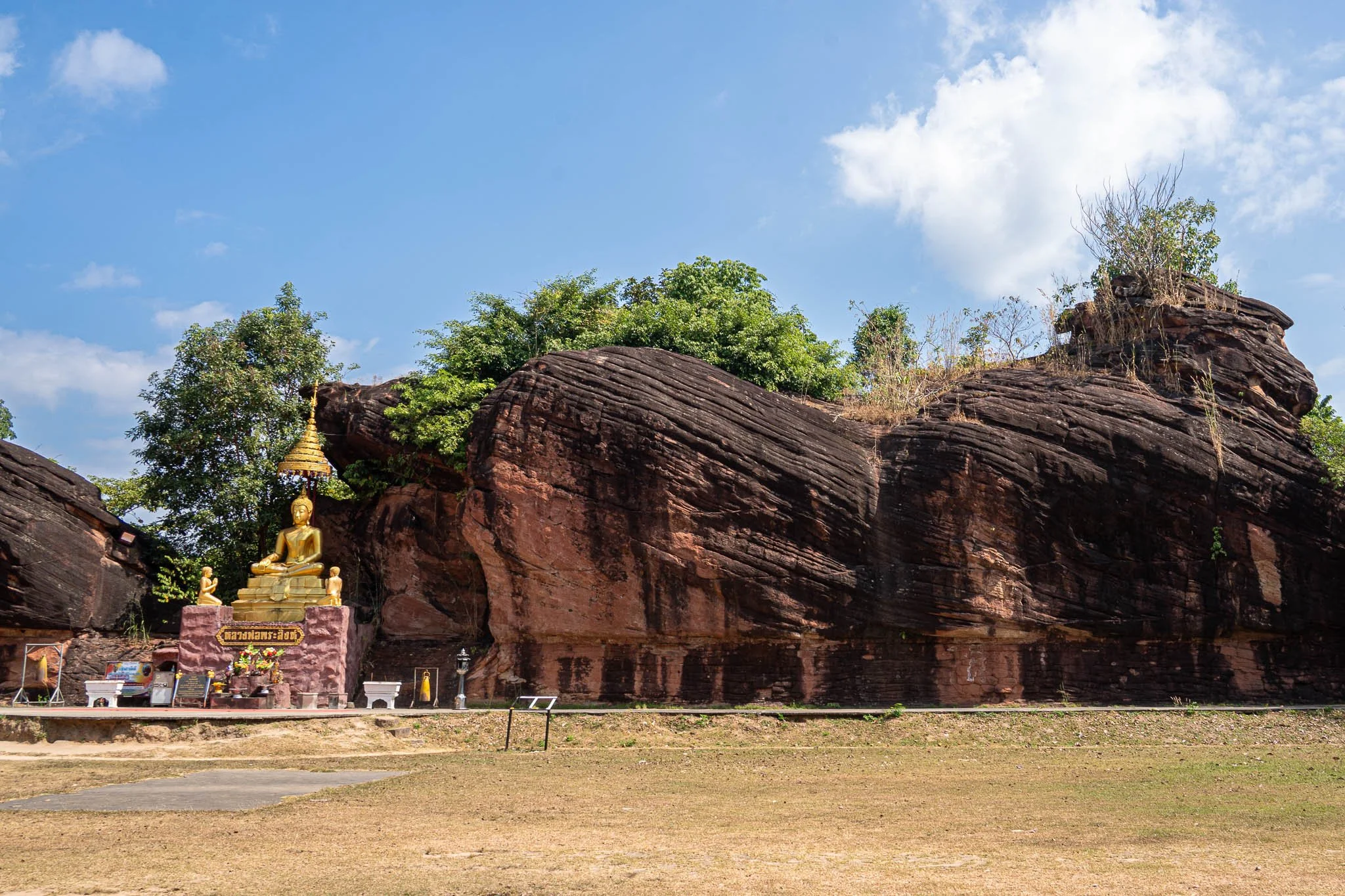 A seated golden Buddha is pictured next to a large rock formation. The rock looks a little like a cat sitting down on its haunches.