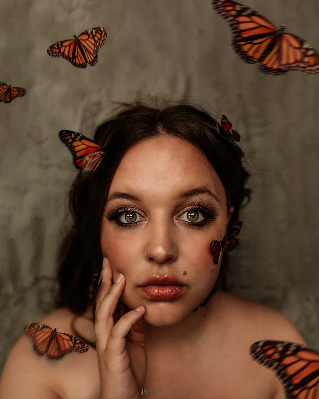 Close-up portrait of a woman with butterfly decorations on her face and shoulders, and Monarch butterflies flying around her.