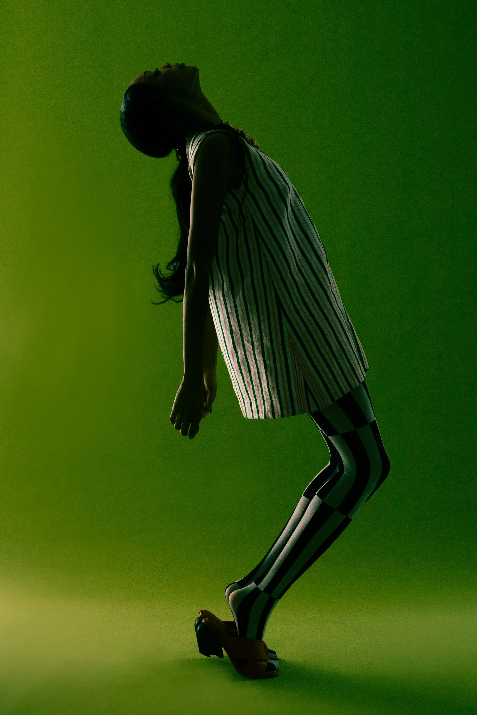 A woman in a striped dress poses with her head tilted back against a green background.