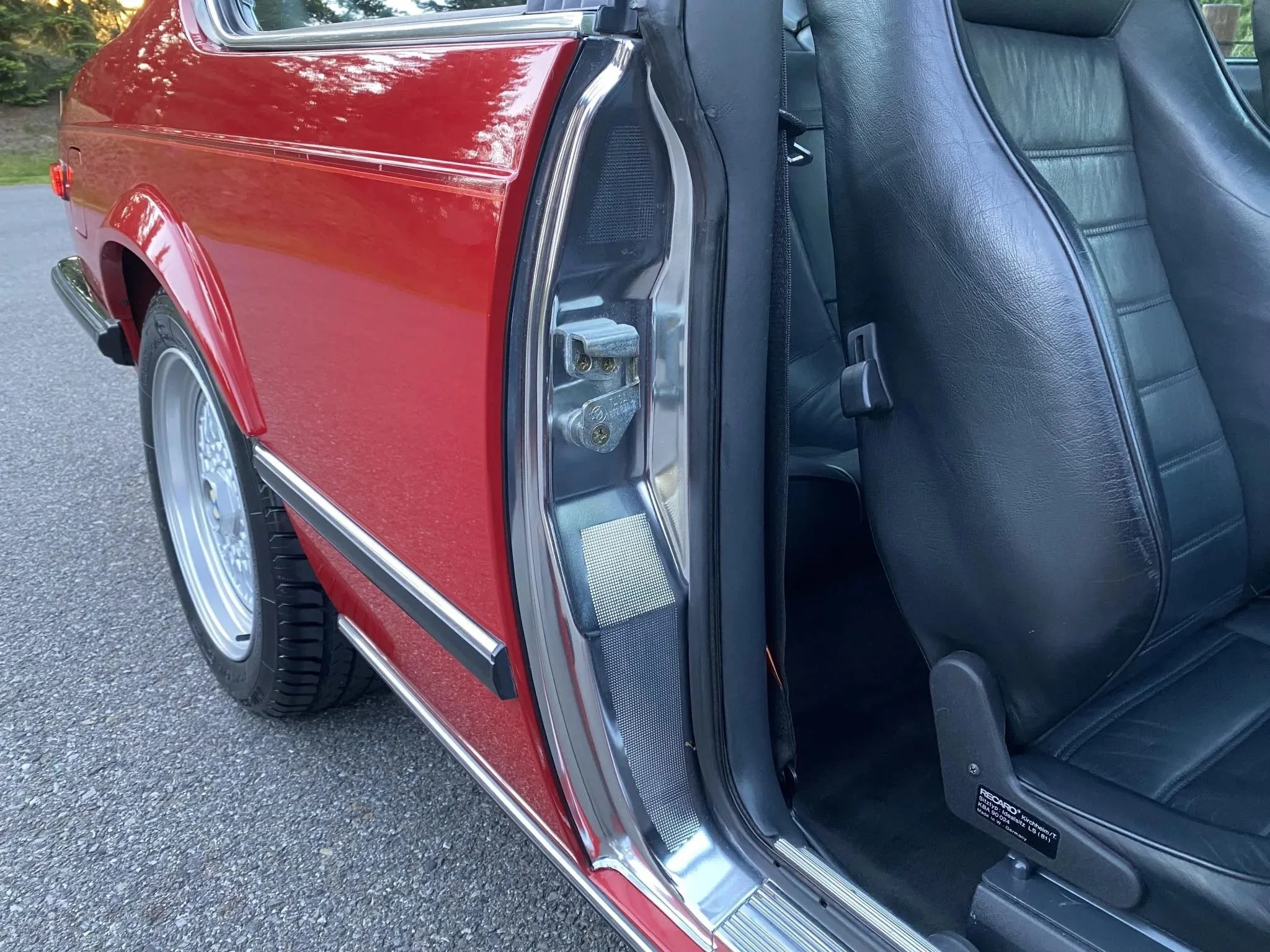Close-up of the side of a red vintage car with a black leather interior and open door showing the seat and door latch.