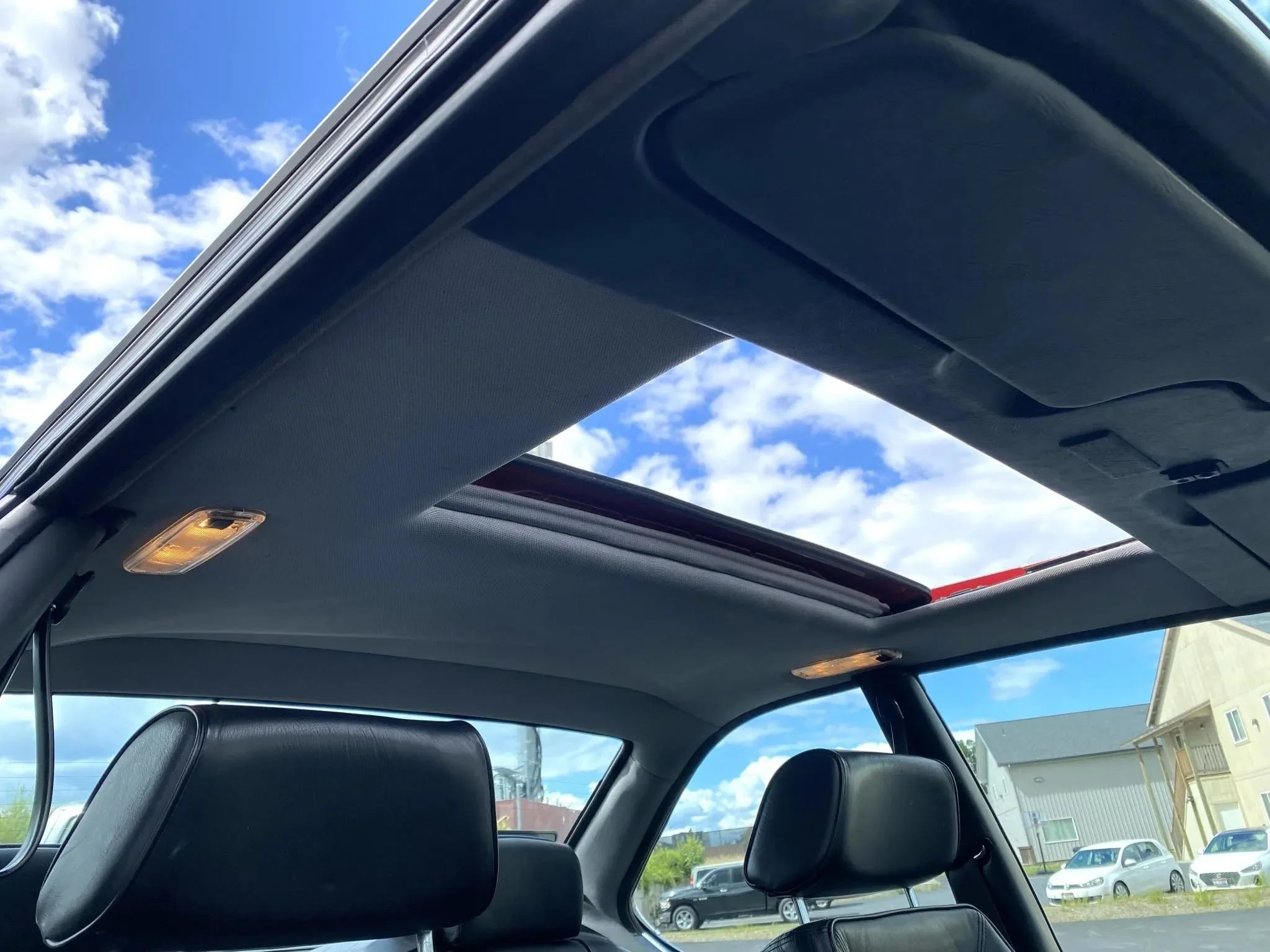 View of the interior of a car with a panoramic sunroof, showing a partly cloudy sky with blue and white clouds.