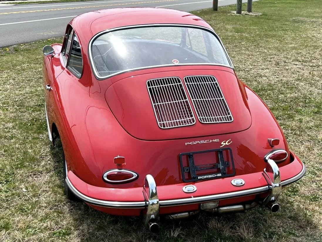 Red vintage Porsche 911 SC parked on grass near a road.