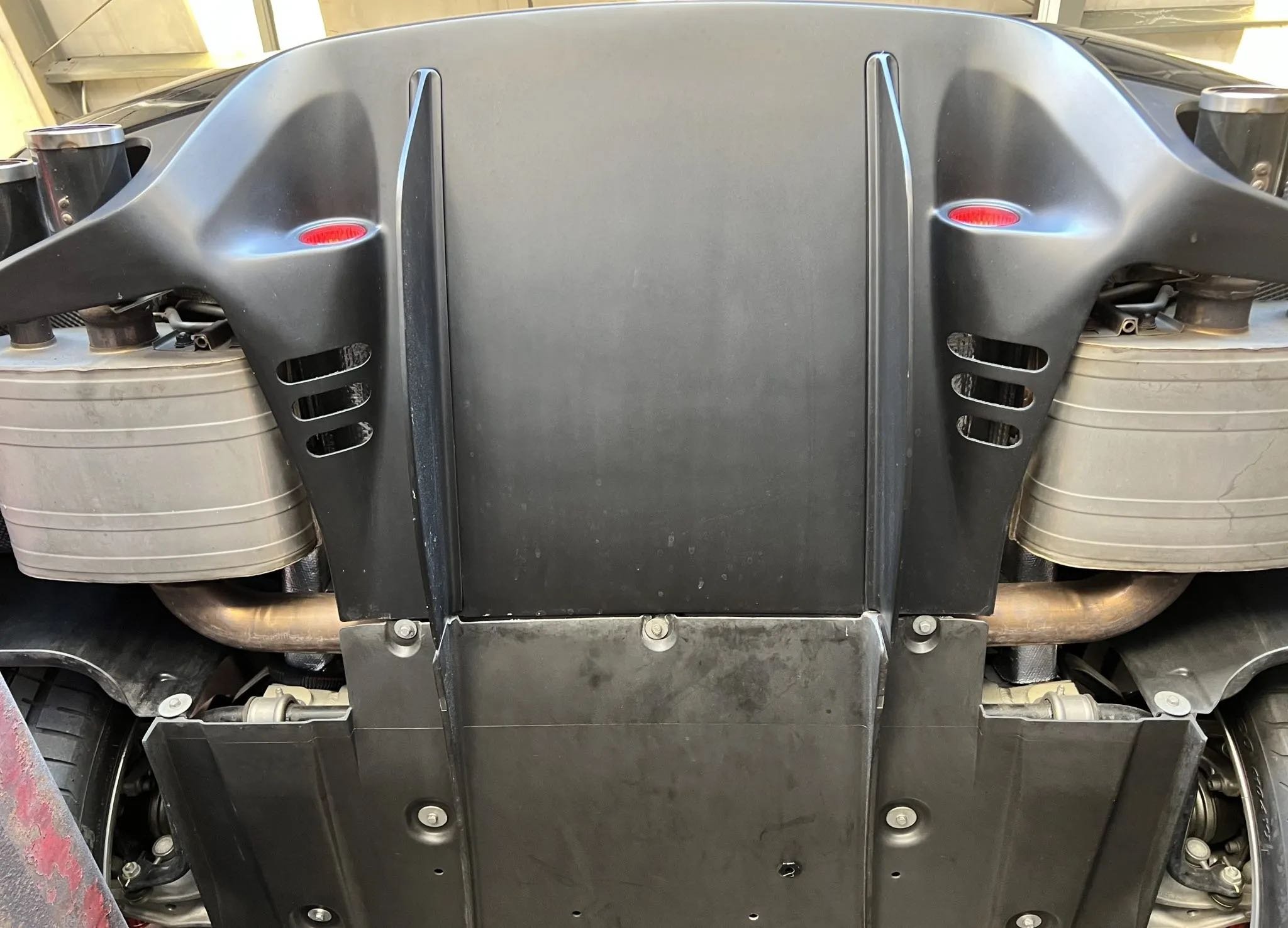 Close-up view of the underside of a vehicle, showing a black plastic protective shield, engine components, and parts of the exhaust system.