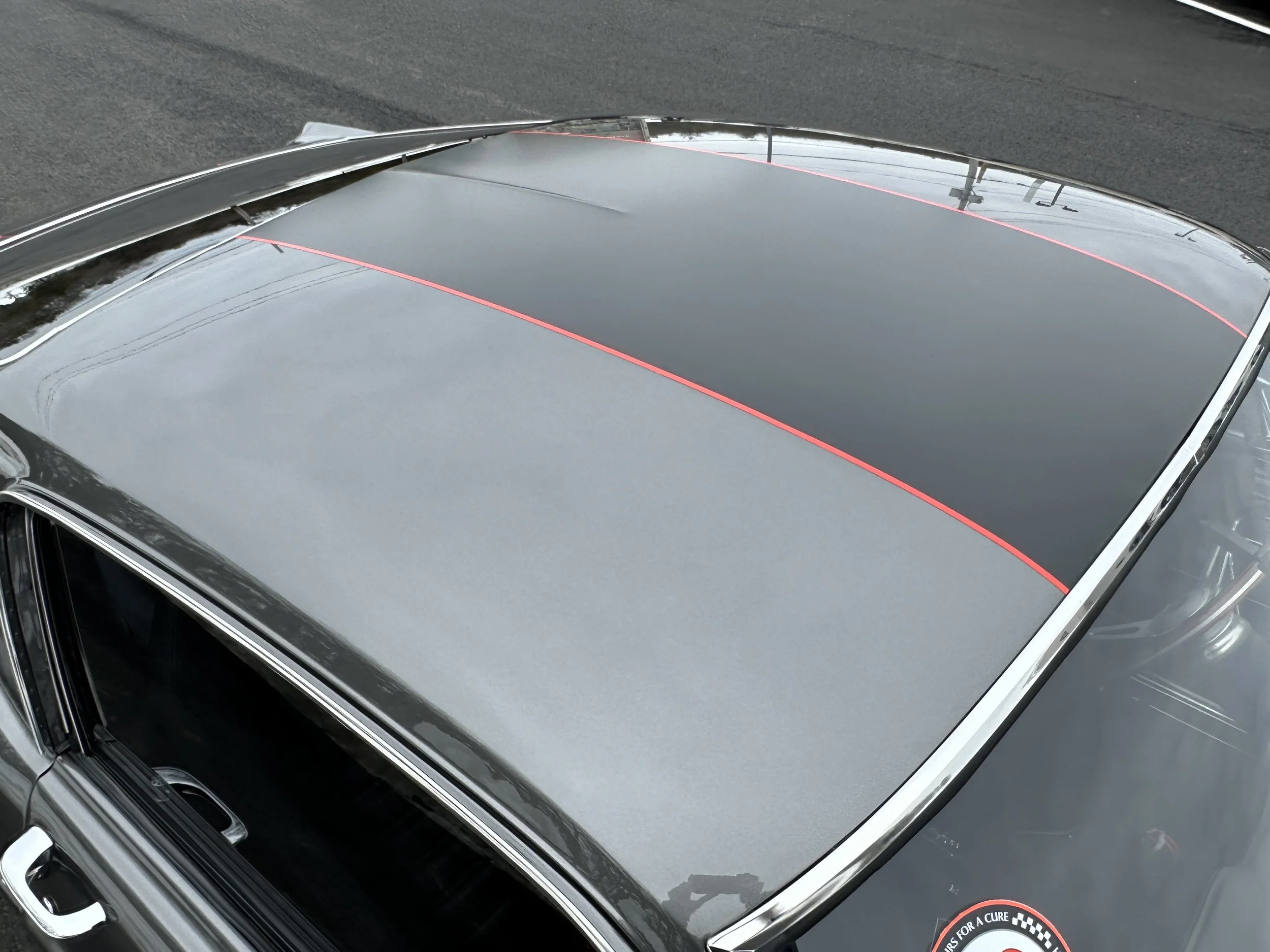 Close-up of a black vintage car's roof with a glossy finish and red racing stripes, parked on a dark paved surface.