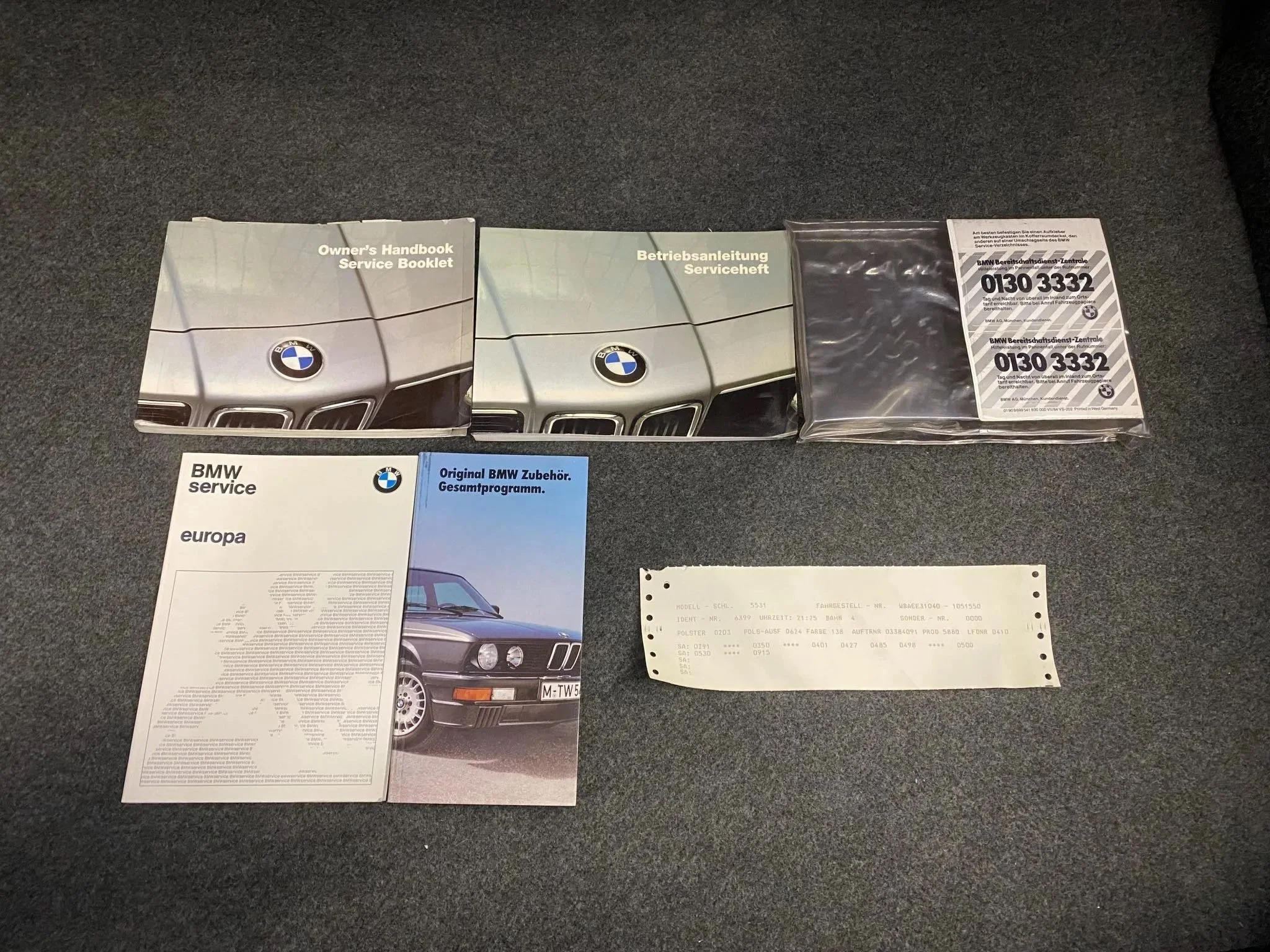 Collection of BMW vehicle manuals, booklets, and a receipt on a carpeted surface, including owners' handbooks, service booklets, and warranty information.