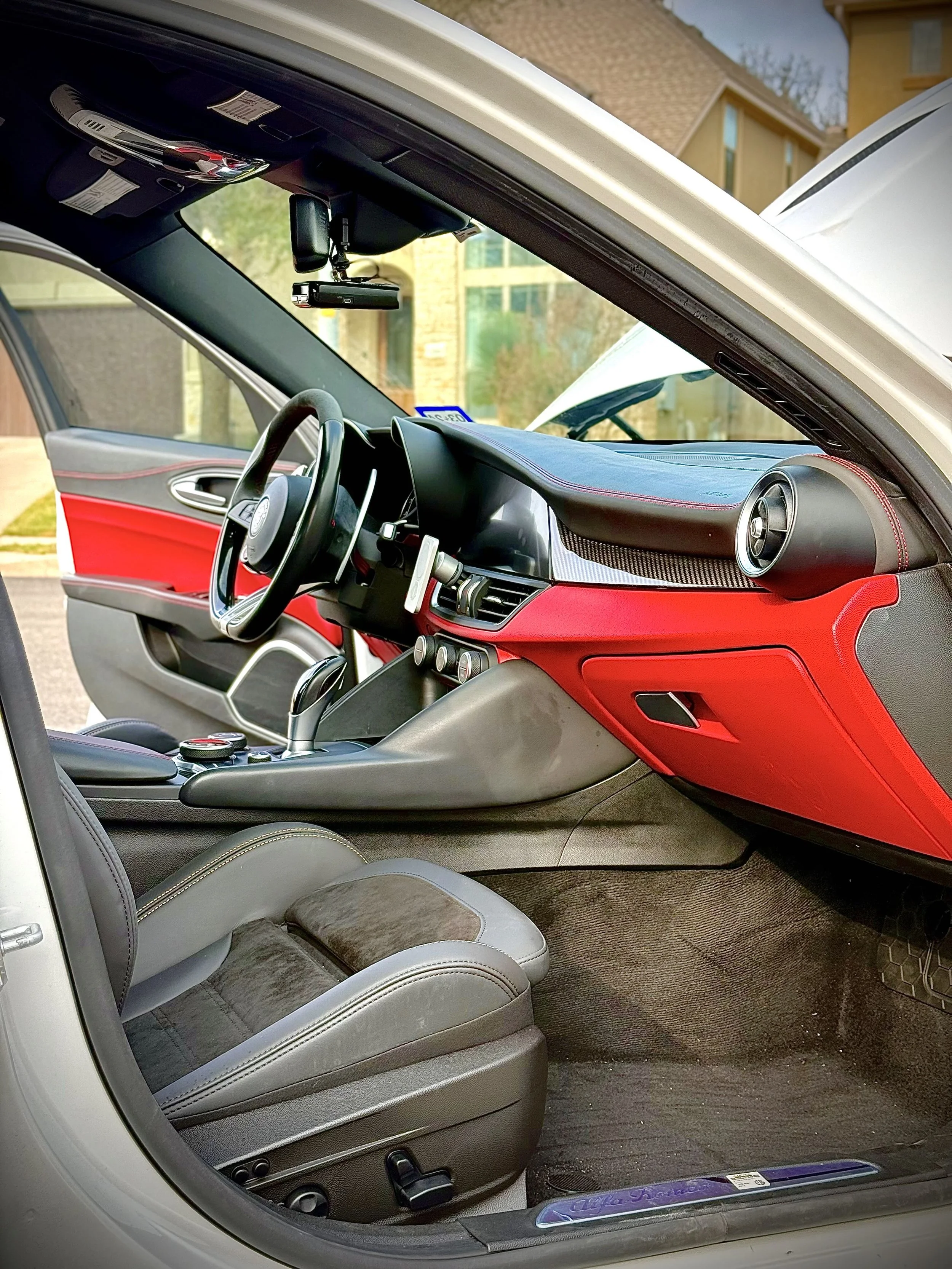 The interior of a modern car showing the driver's seat, steering wheel, dashboard, and part of the open passenger door.