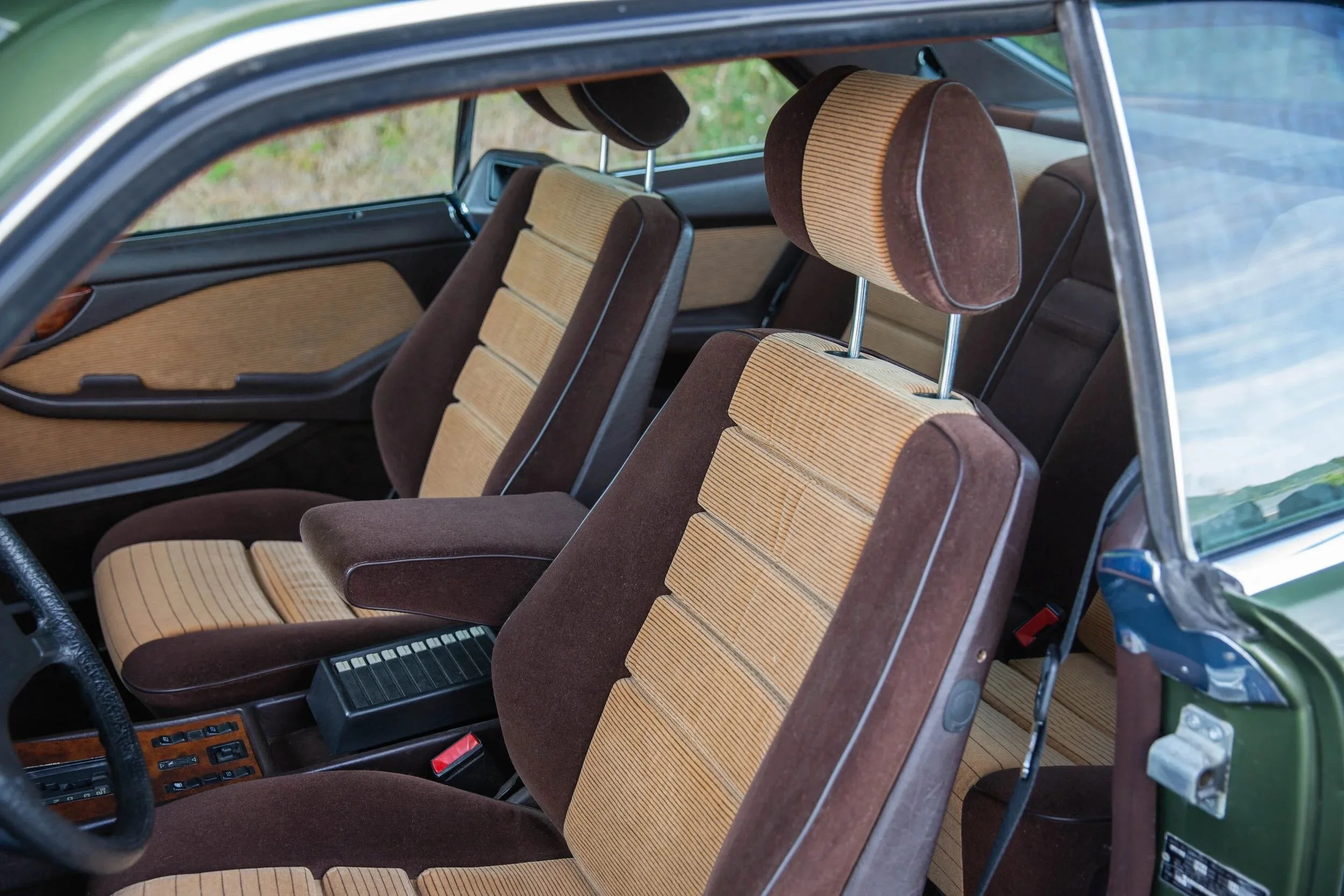 Interior of a vintage car showing front and back seats with brown and beige fabric upholstery.