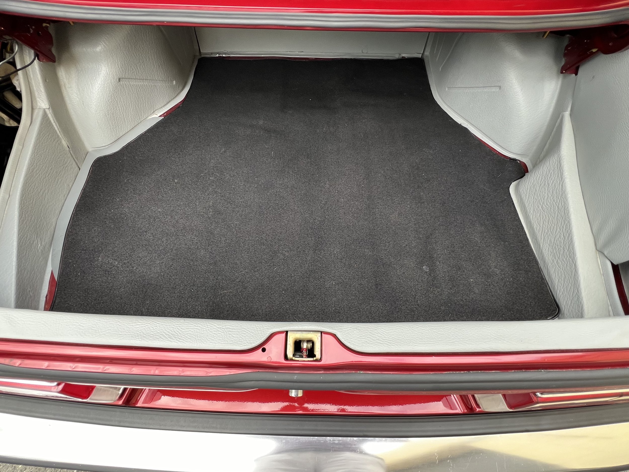 The trunk of a red 1977 BMW 630 csi with beige interior and a black carpeted floor.
