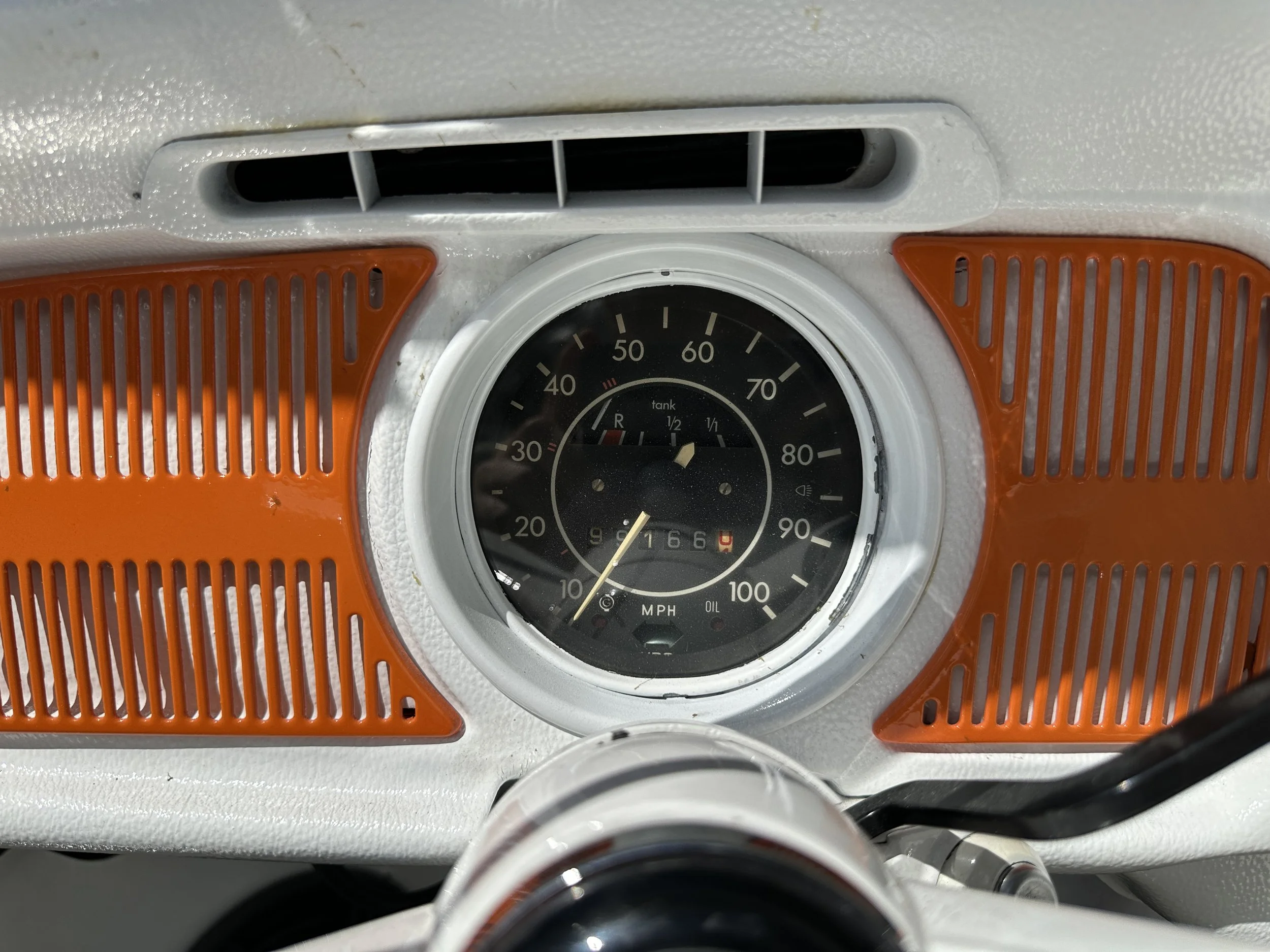 Close-up of a vintage dashboard featuring a speedometer, fuel gauge, oil indicator, and orange vents.