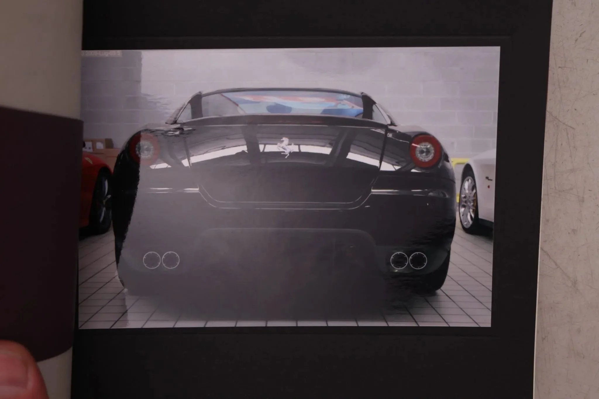 Photo of a black Ferrari sports car viewed from the rear, parked indoors with red and yellow cars nearby.