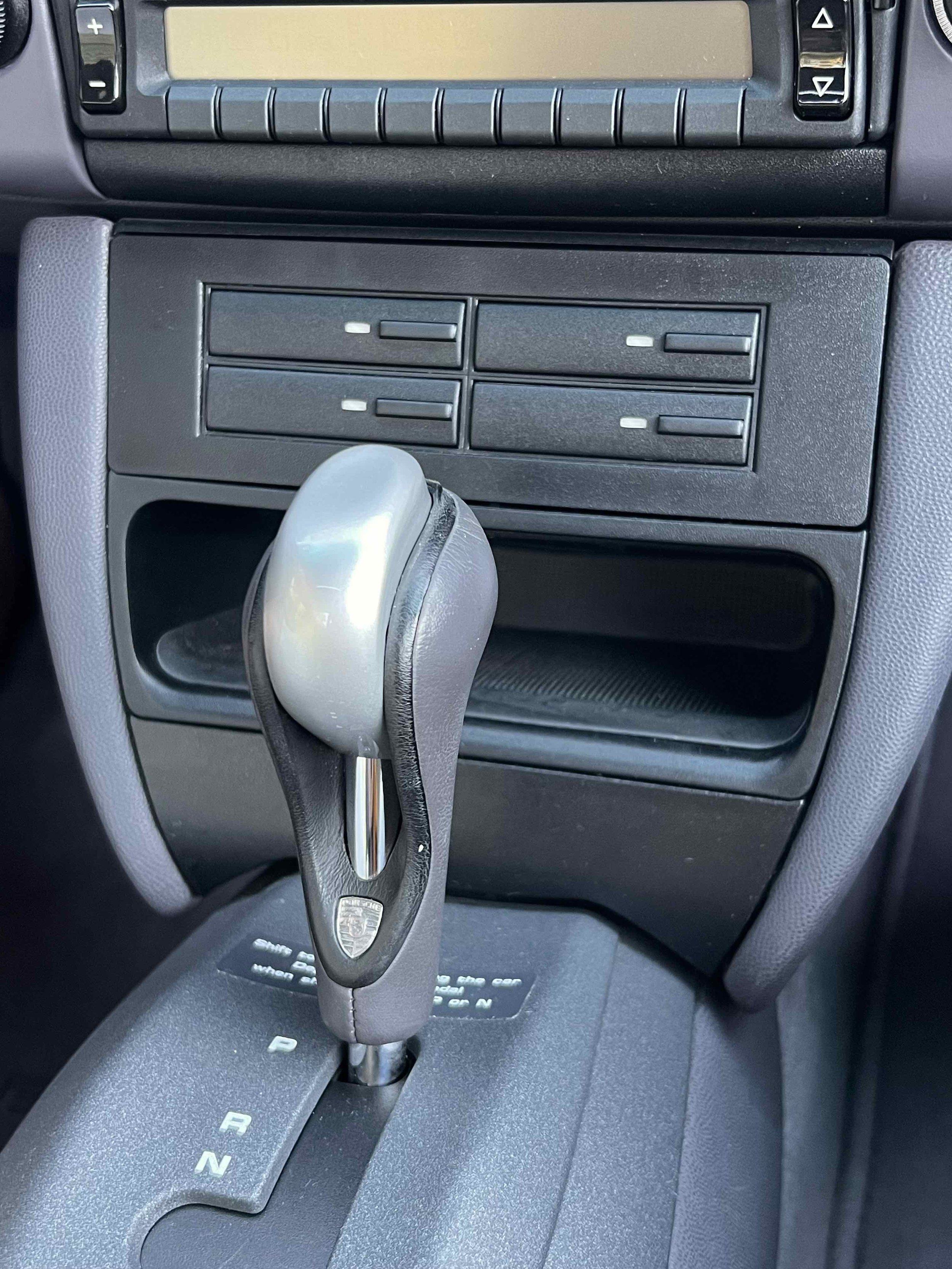 Interior view of a car dashboard showing the gear shifter, with the letters P, R, N, and D visible, and additional controls and compartments above.