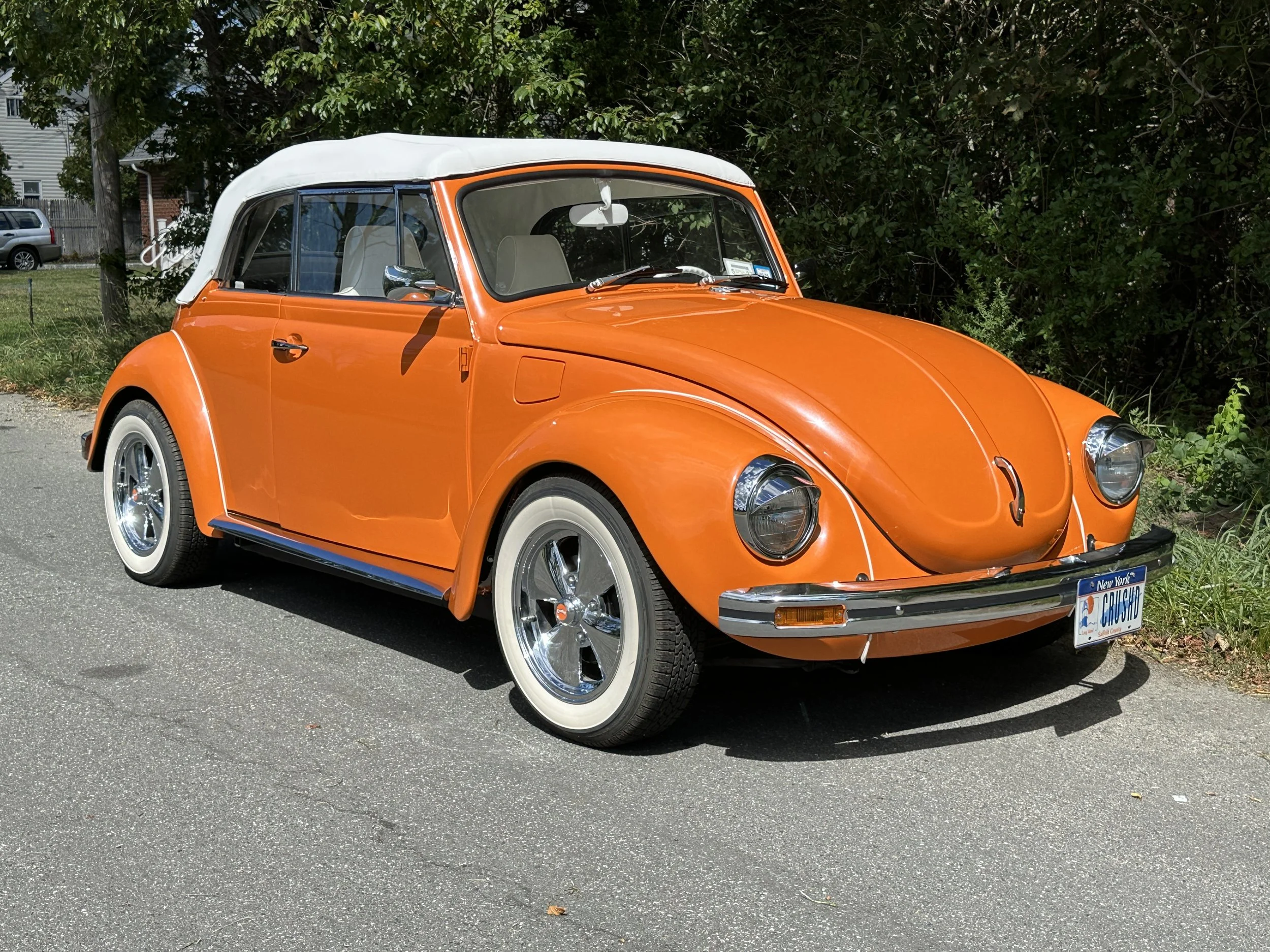 Orange vintage Volkswagen Beetle convertible with white roof parked on a street.