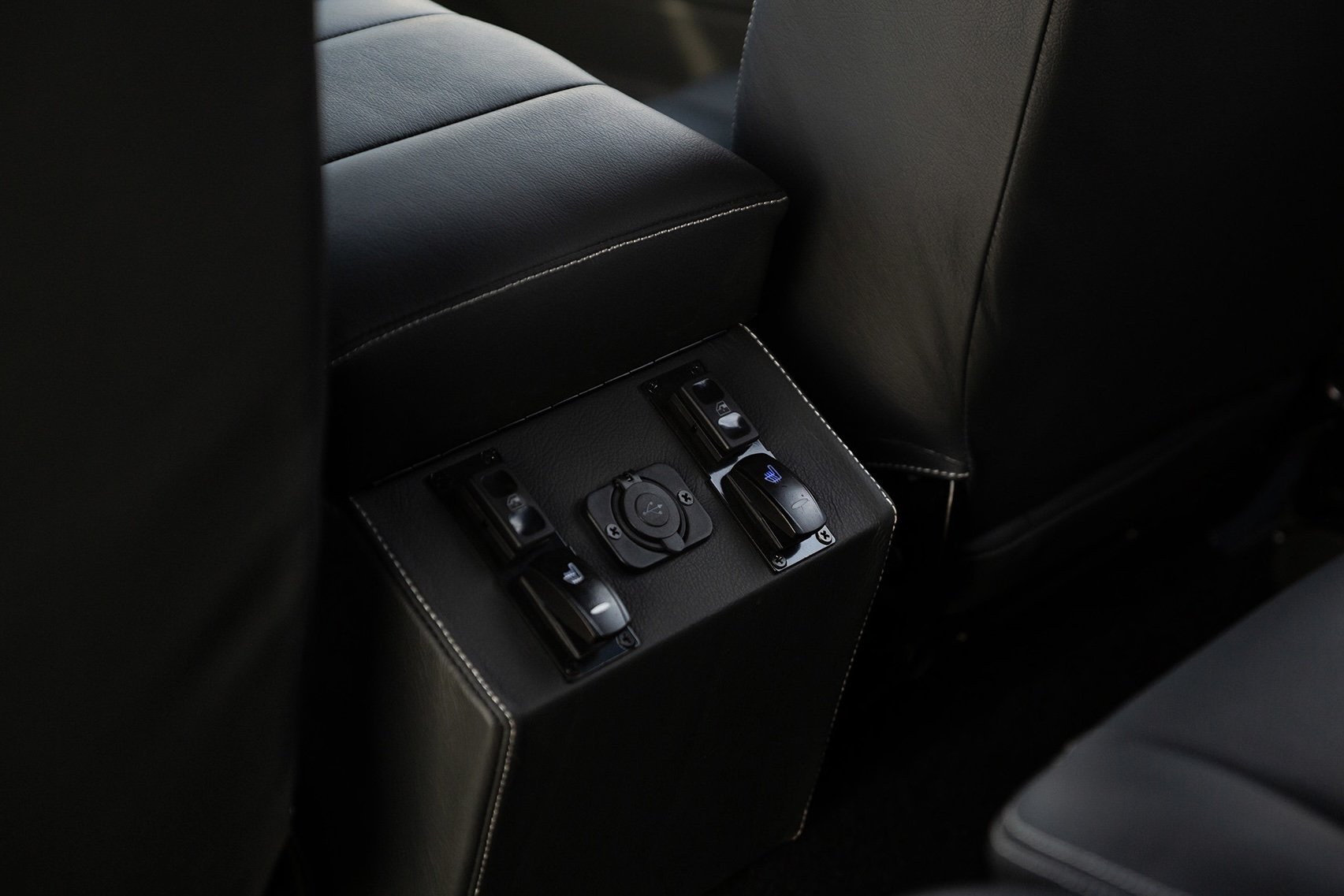 The back seat of a car showing control buttons for seat adjustment and climate control on a central panel.