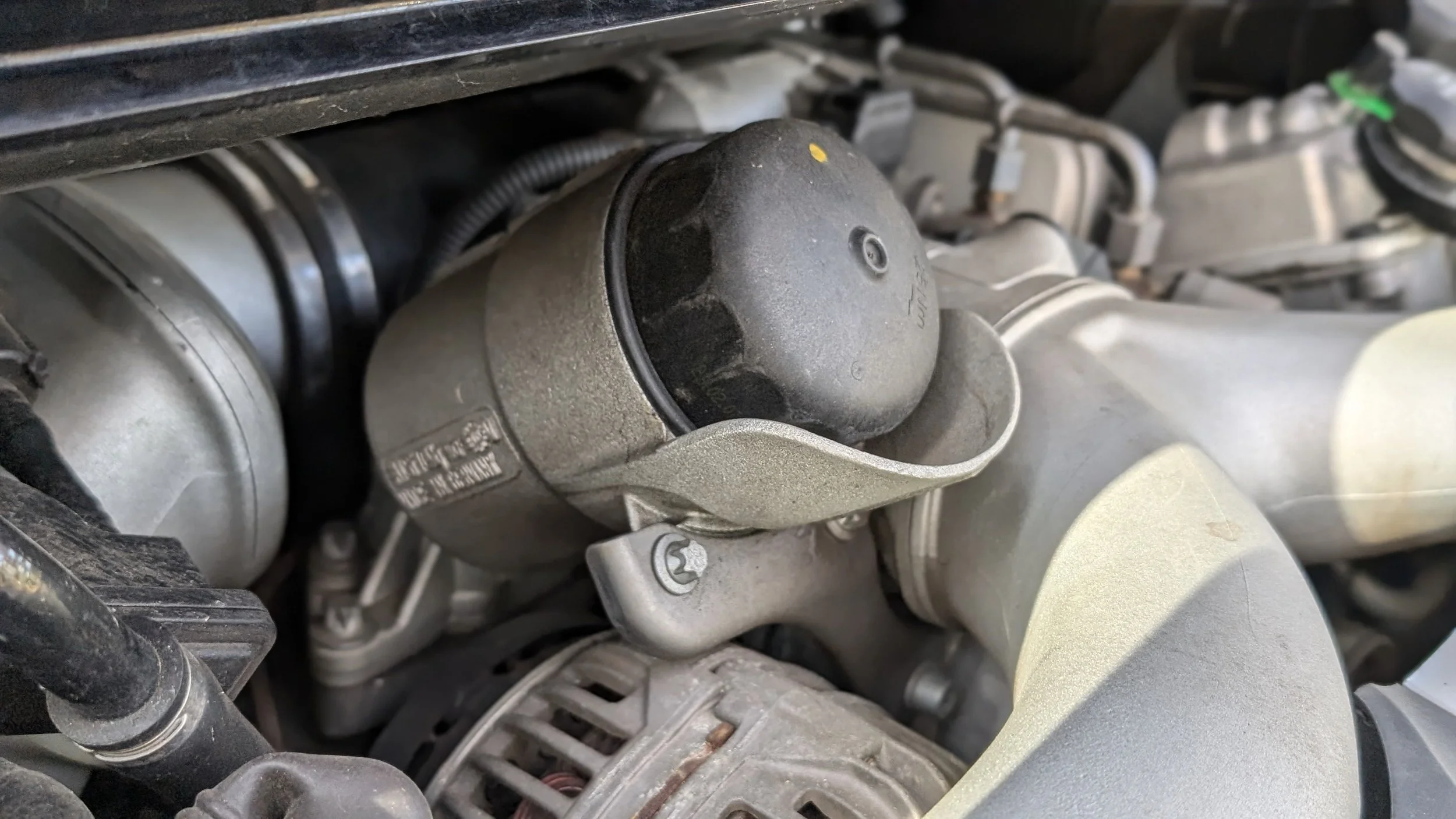 Close-up of a car engine component with a black rubber cap, showing metallic parts and various engine parts around it.