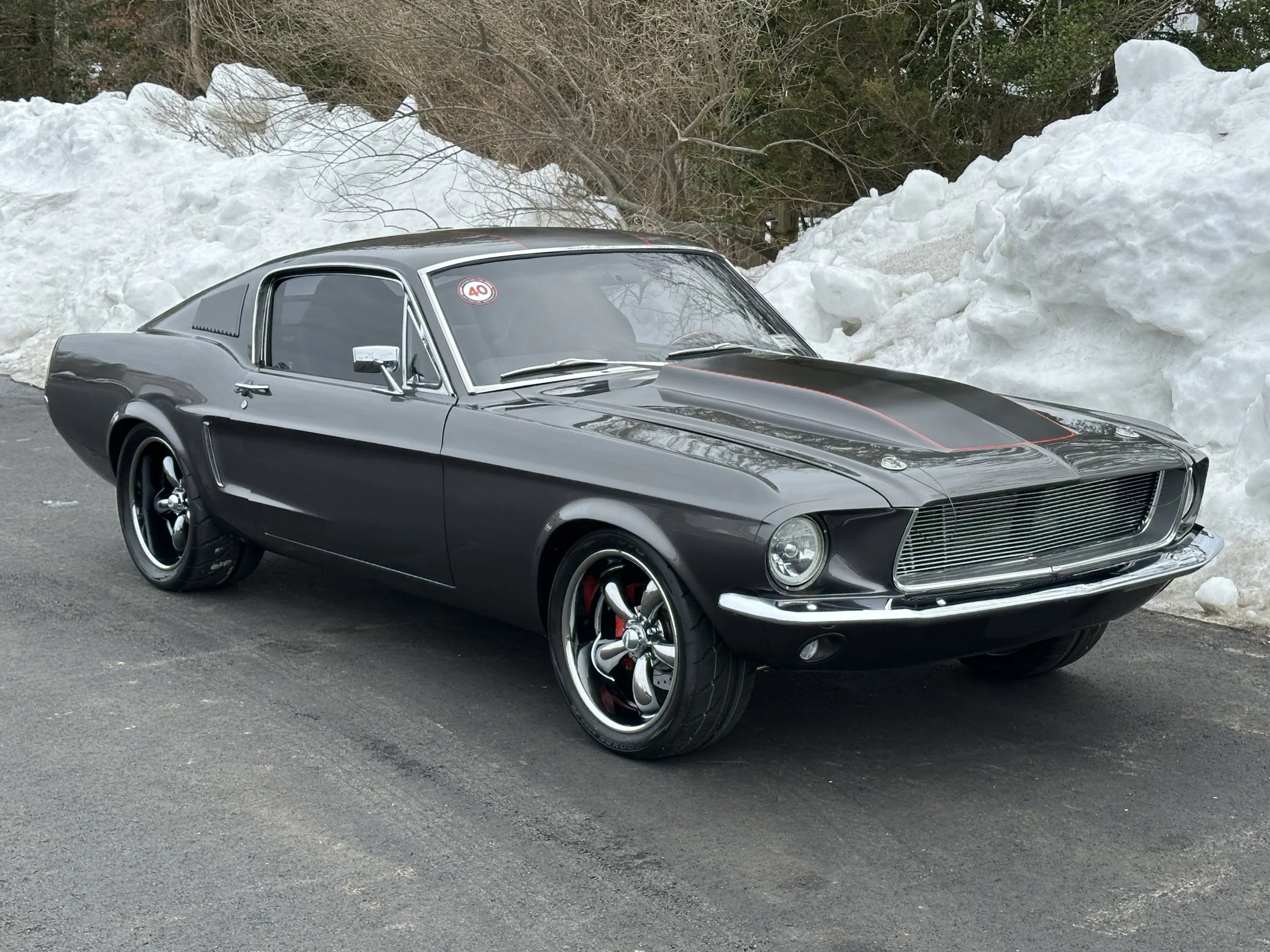 A black vintage muscle car parked on the side of a road with snow piled behind it.