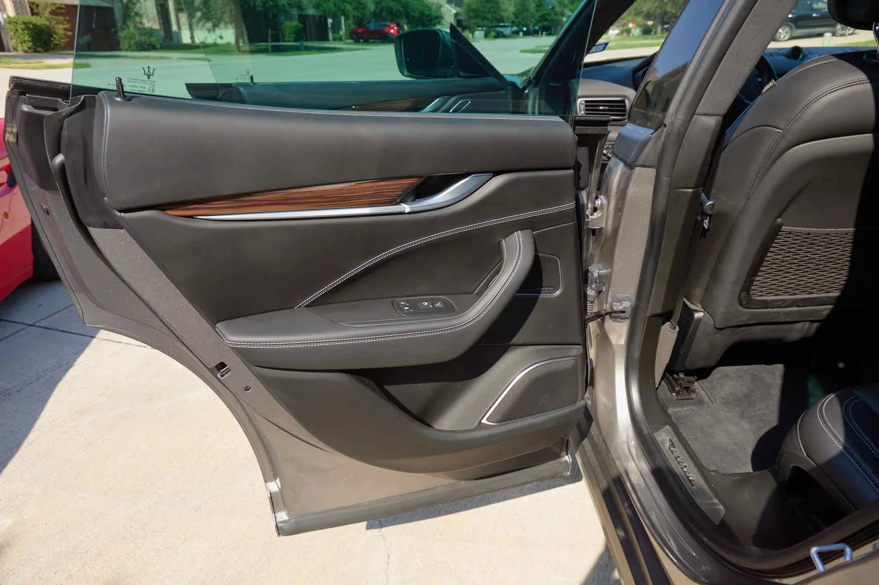 The image shows the interior and open rear door of a black luxury SUV, revealing the front and back seats, seat controls, and a wood trim detail on the door panel.