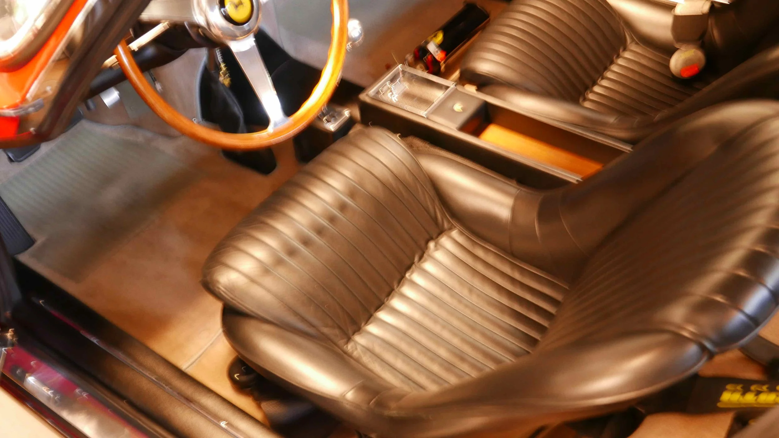 View of a classic car interior with brown leather bucket seats, wooden steering wheel, and center console with gear shift.