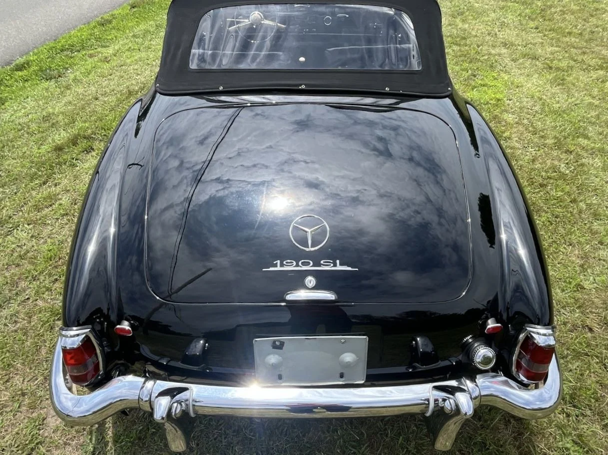 Rear view of a black vintage Mercedes-Benz 190 SL car on grass, displaying the Mercedes-Benz logo and model name on the trunk.