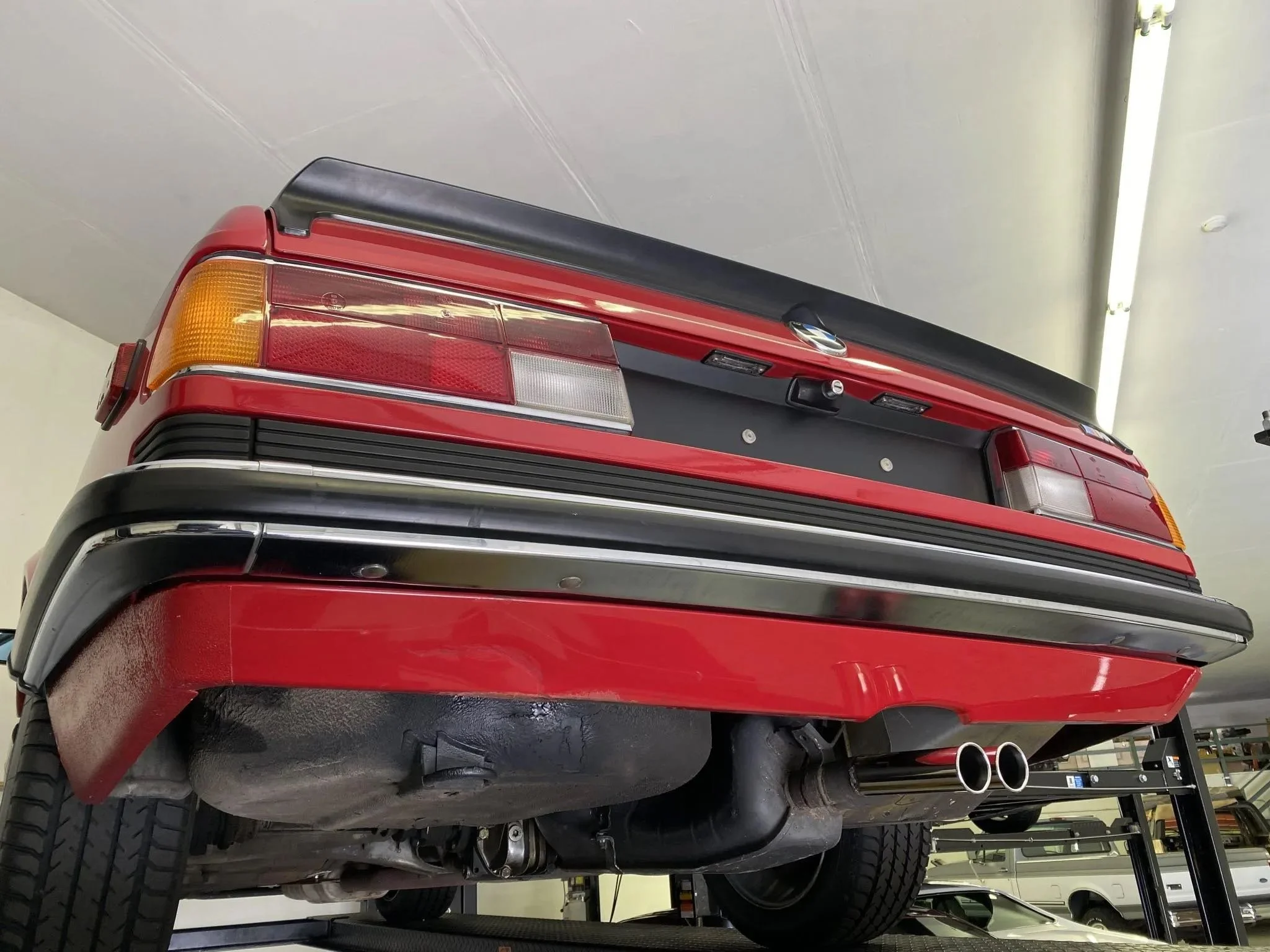 Rear view of a red vintage car showing tail lights, bumper, exhaust pipes, and undercarriage